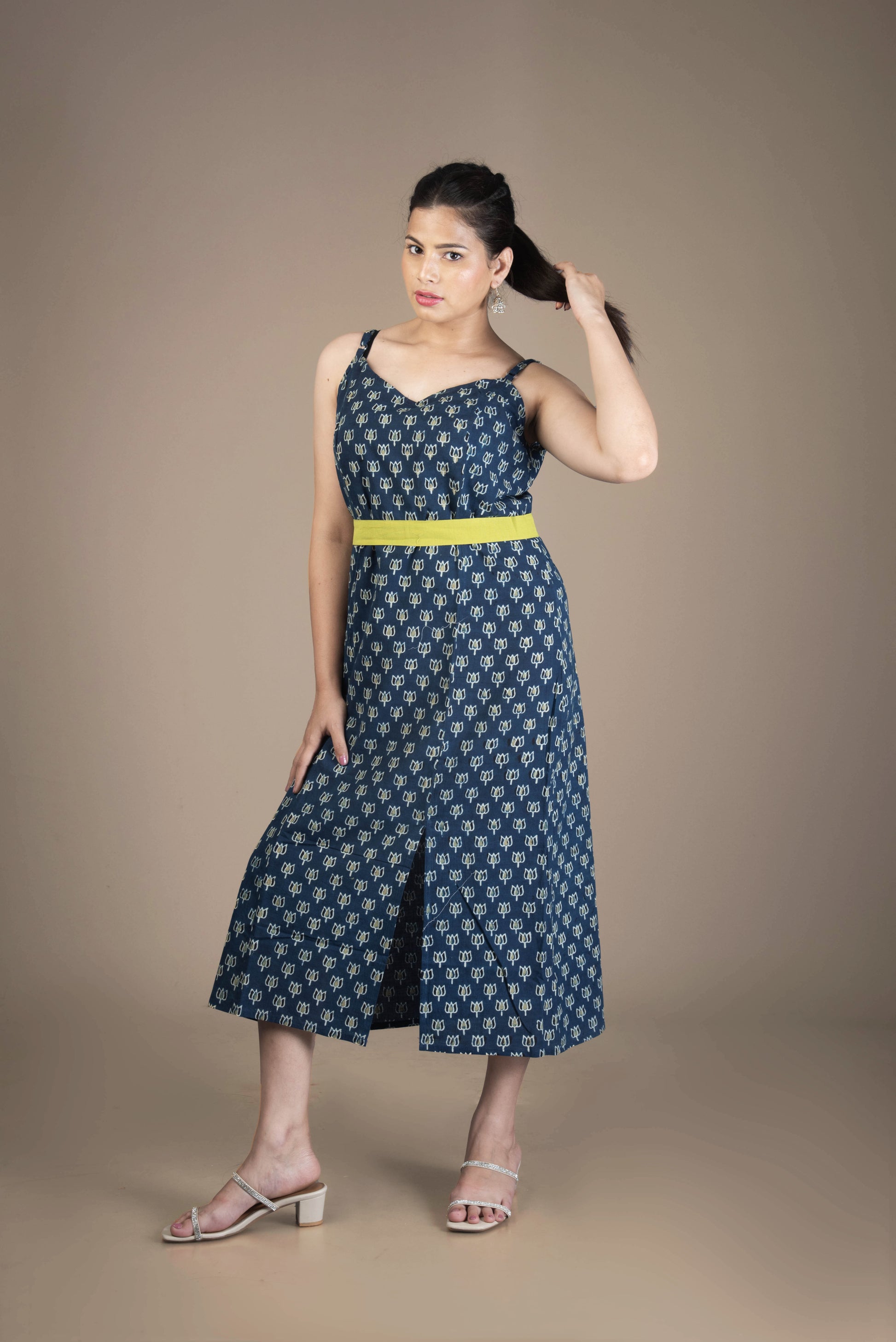 Woman wearing a blue patterned dress with a yellow belt against a brown background