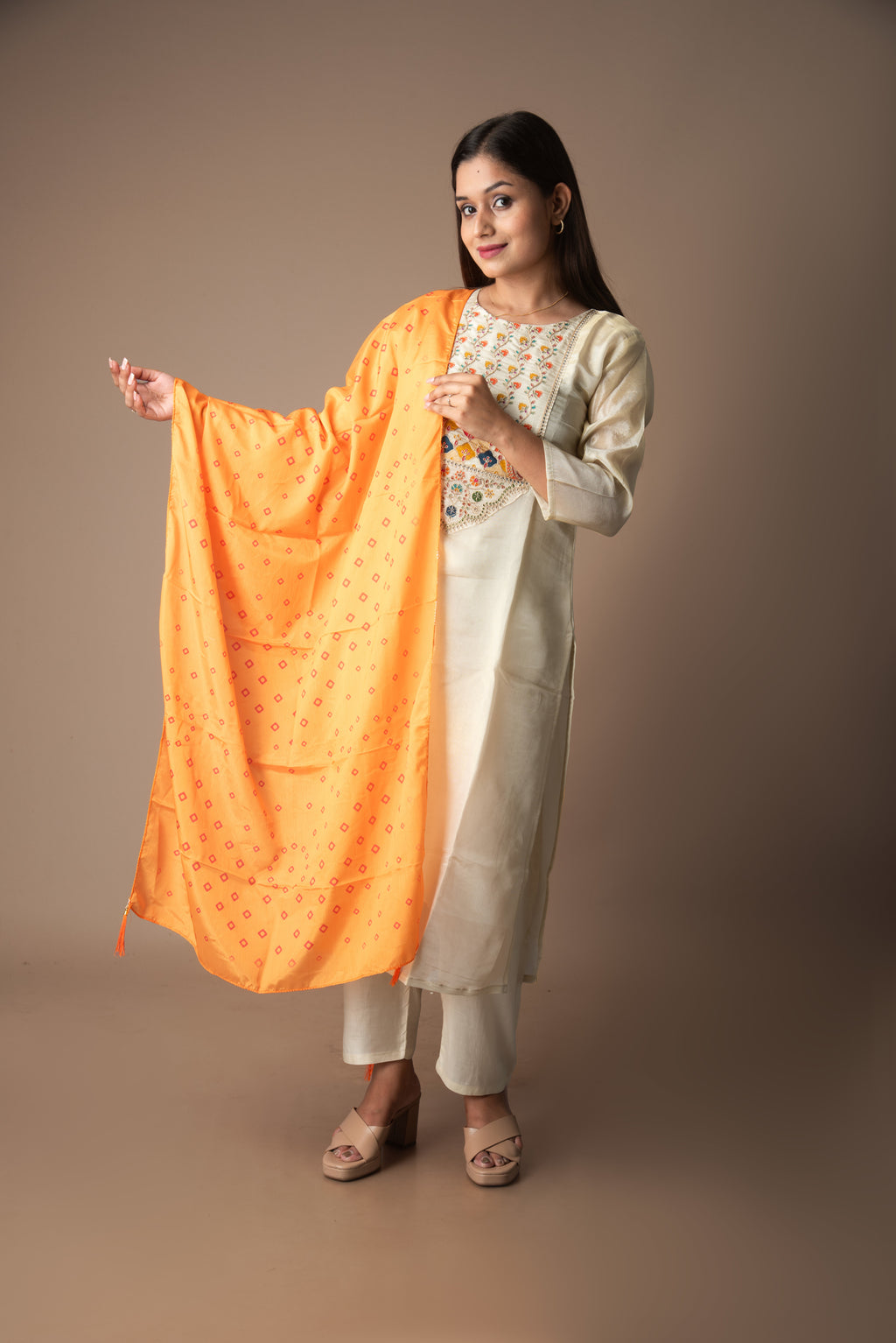 Woman holding an orange dupatta against a plain background