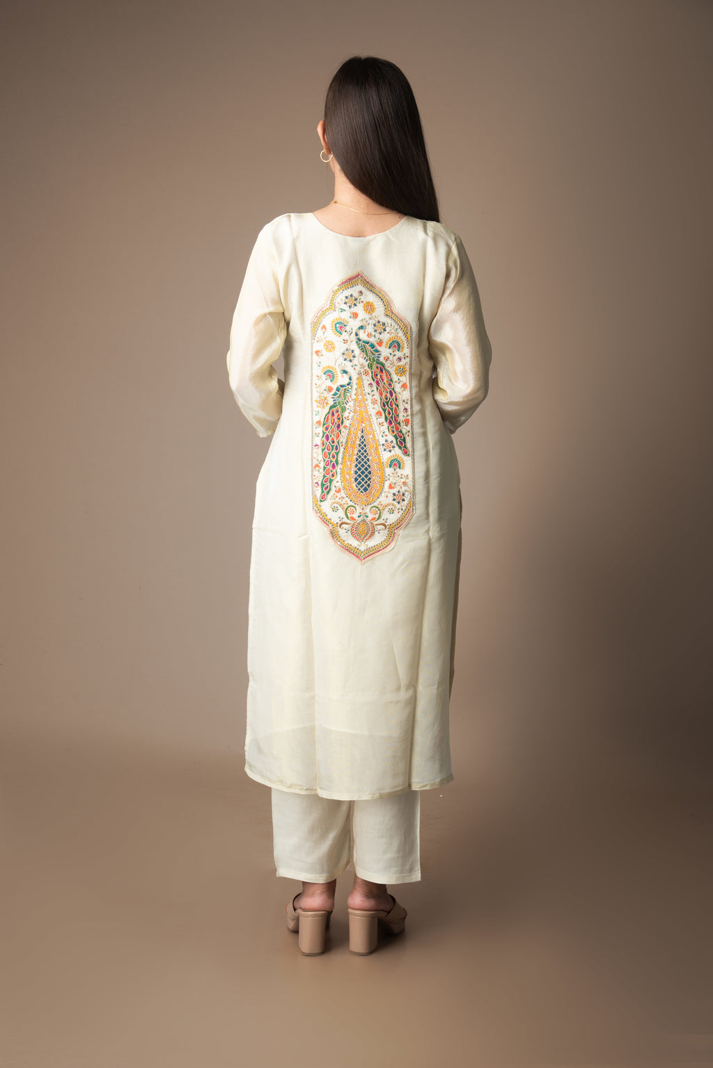 Woman wearing a cream-colored kurta with intricate embroidery on the back against a brown background