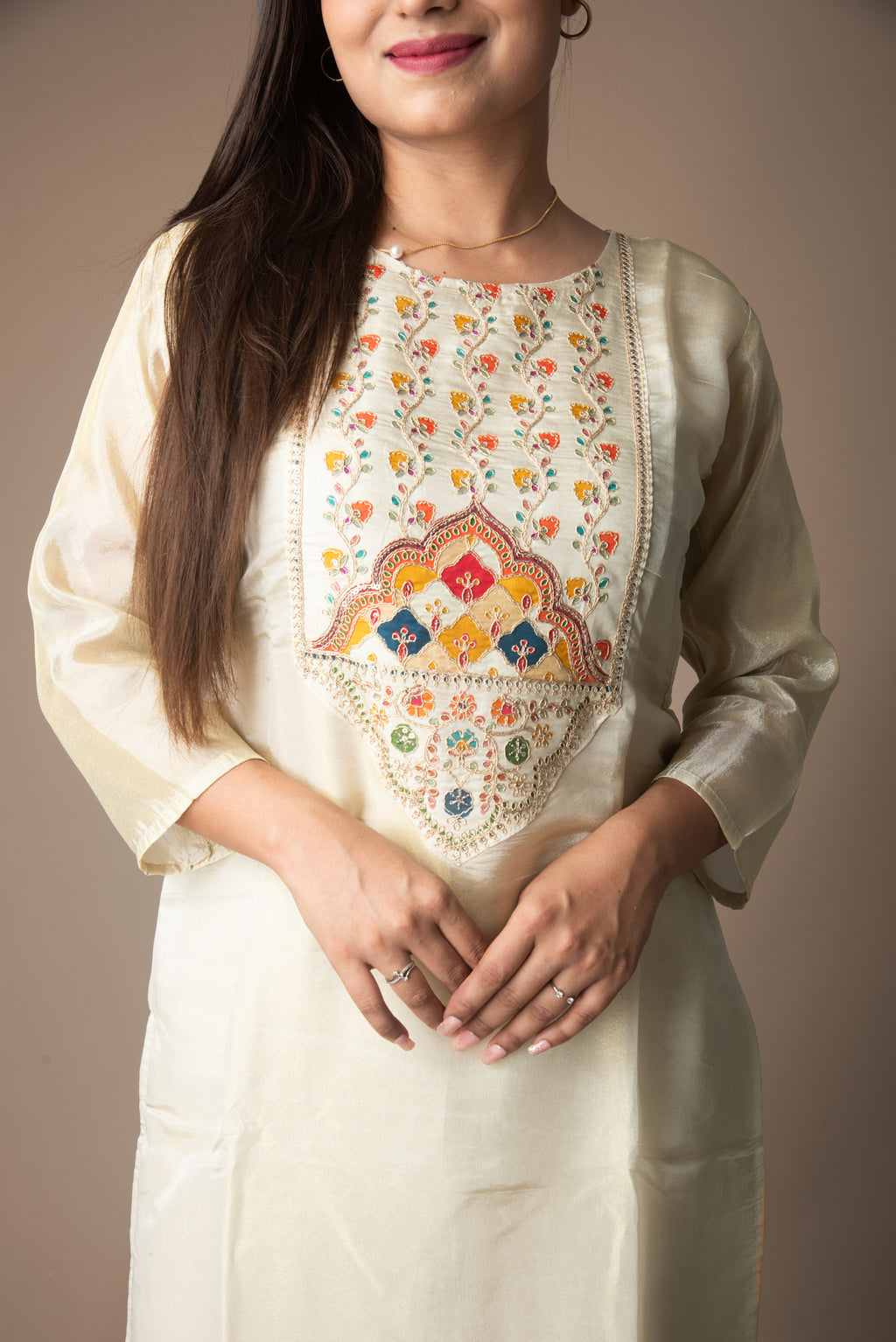 Woman wearing a cream kurta with intricate multicolor embroidery on a plain background