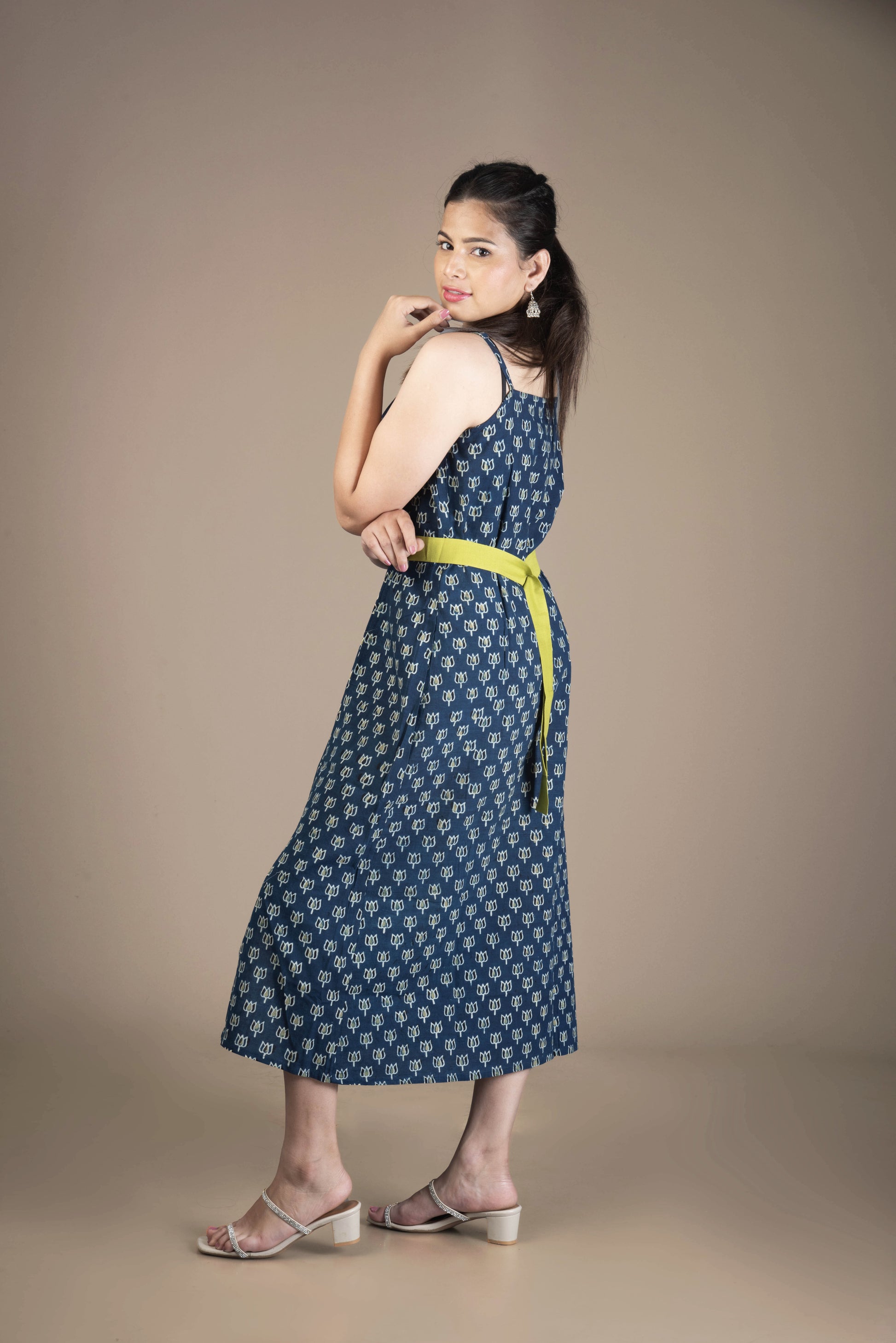 Woman wearing a blue patterned dress with a yellow belt against a brown background