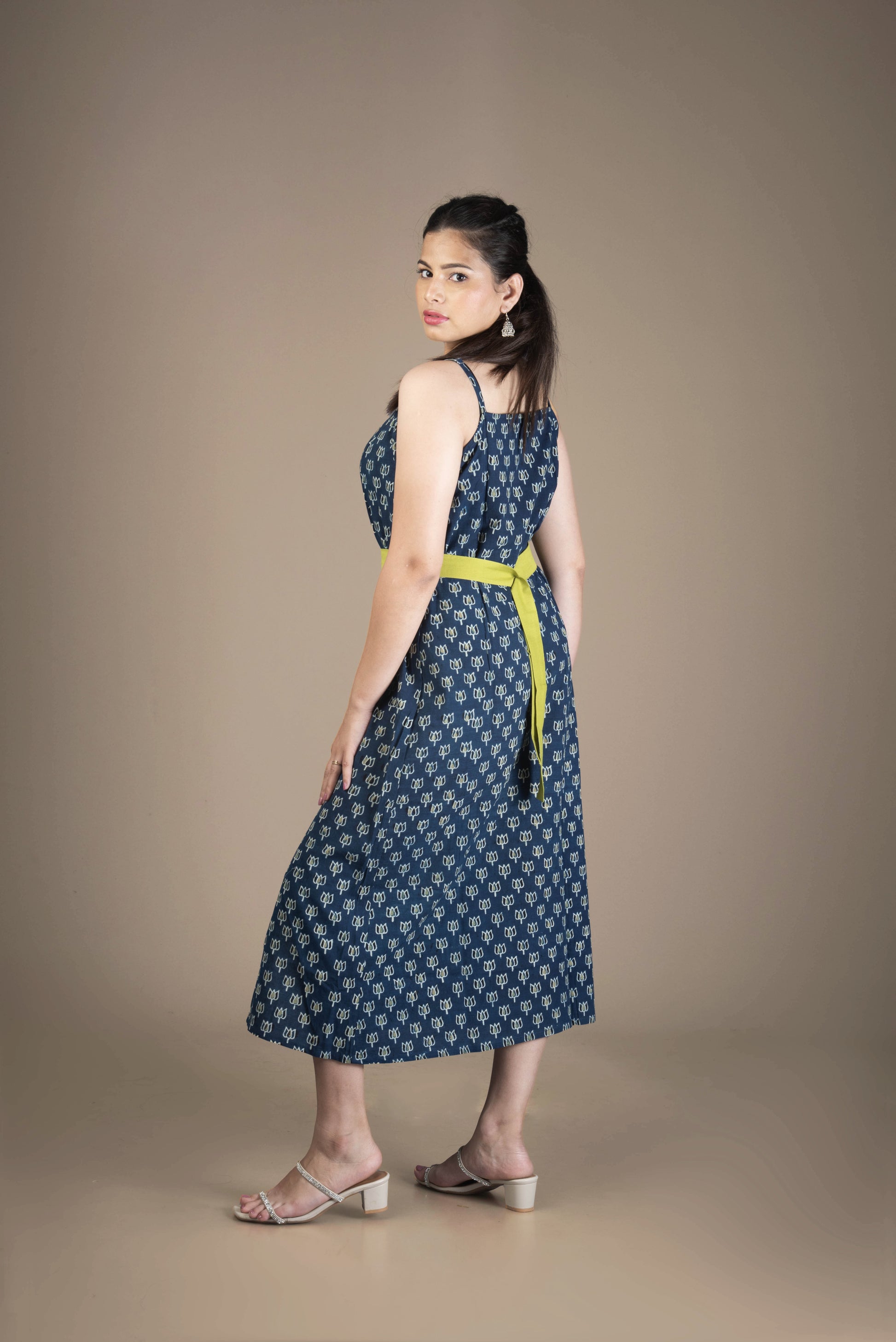 Woman wearing a blue patterned dress with a yellow belt against a brown background
