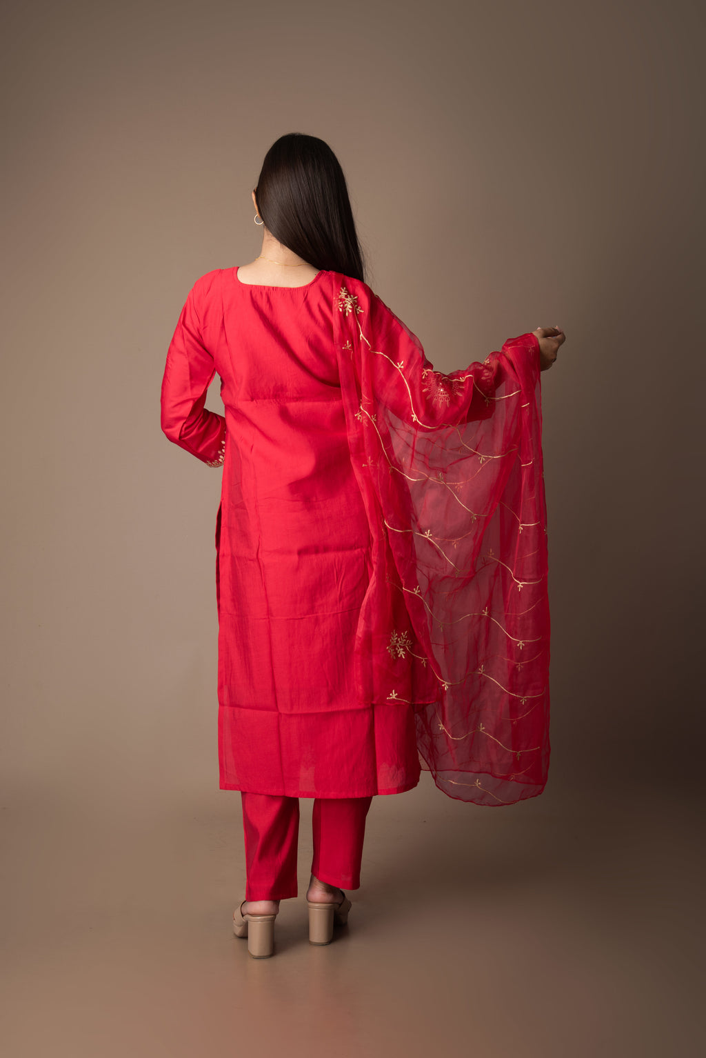 Woman in a red traditional outfit with a sheer dupatta against a brown background