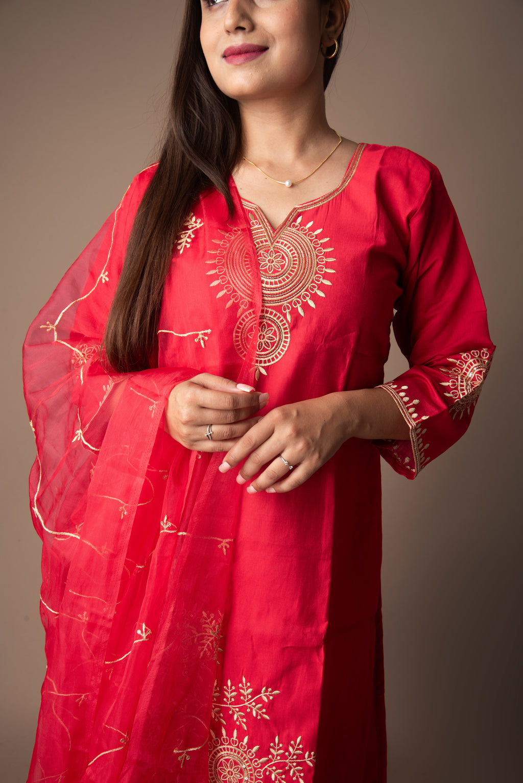 Woman wearing a red embroidered traditional outfit against a neutral background