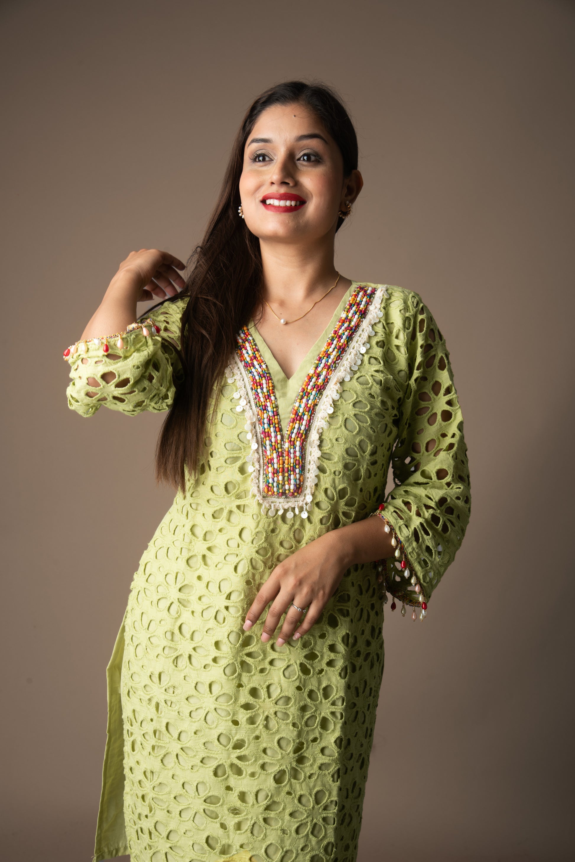 Woman wearing a green traditional outfit with intricate patterns and bead details on a brown background