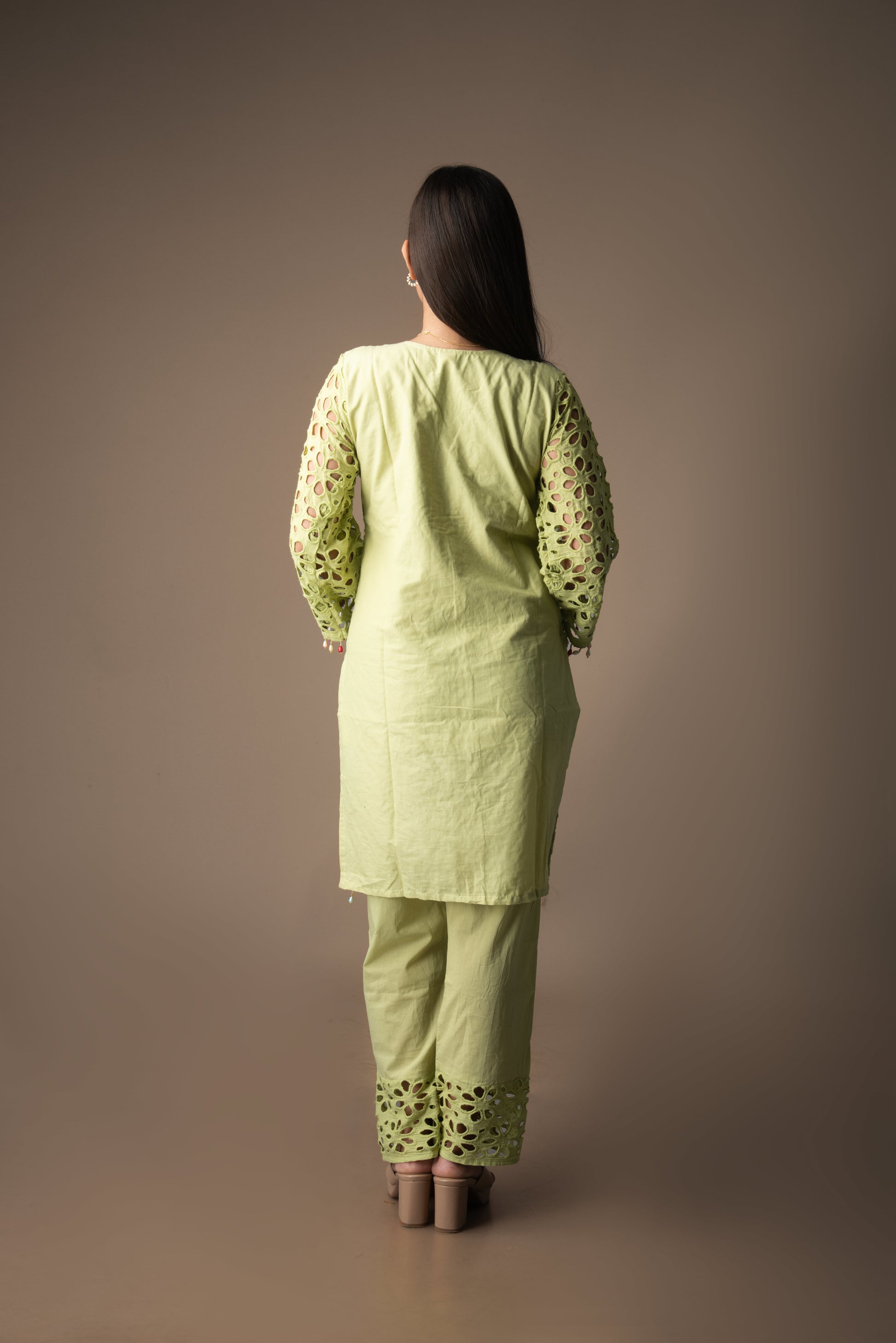 Woman wearing a light green traditional outfit with floral patterns on a brown background