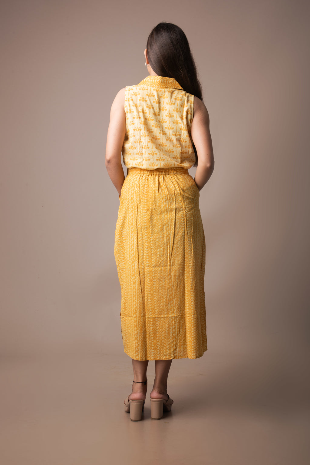 Woman wearing a yellow sleeveless top and skirt against a brown background