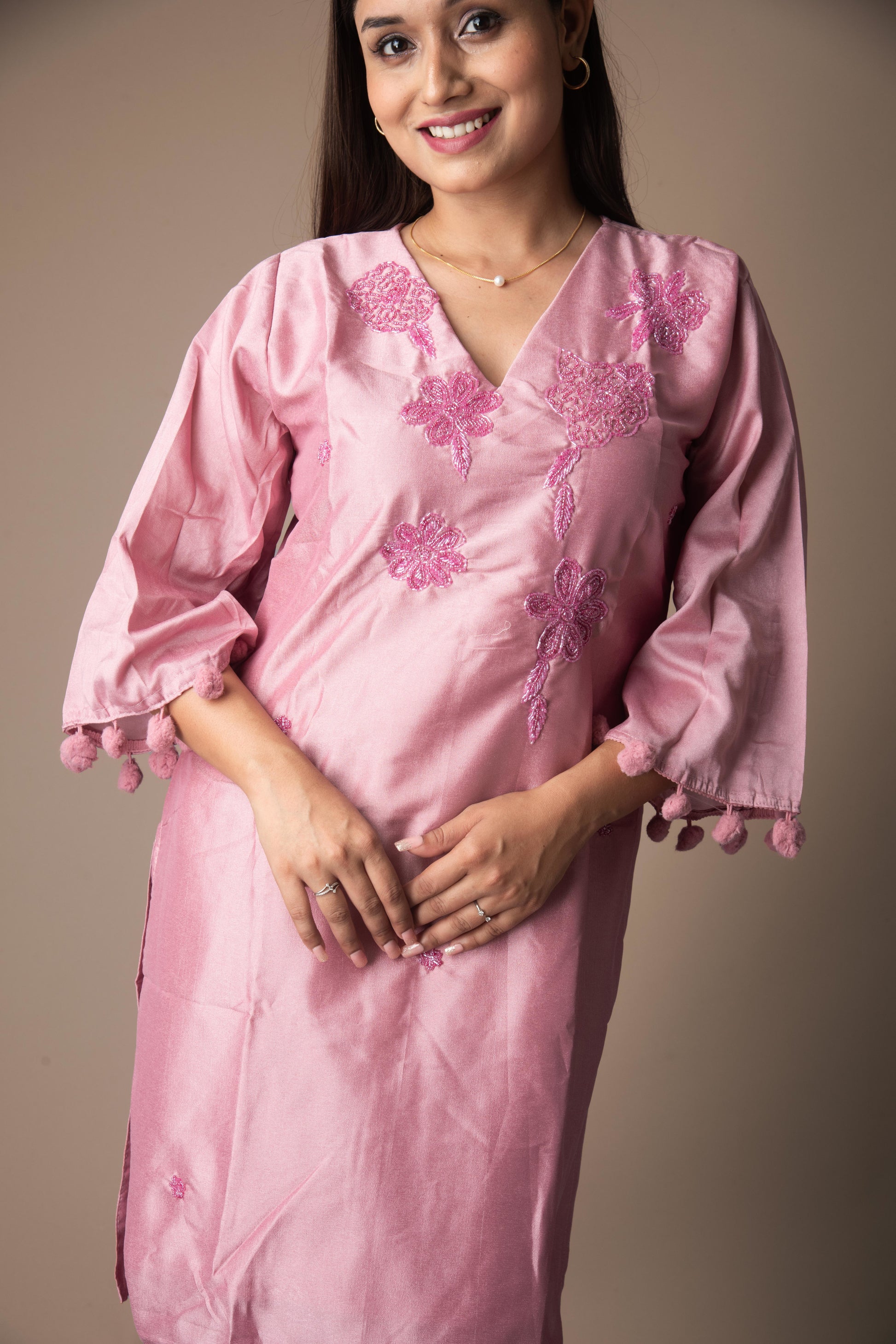 Woman wearing a pink embroidered dress against a plain background
