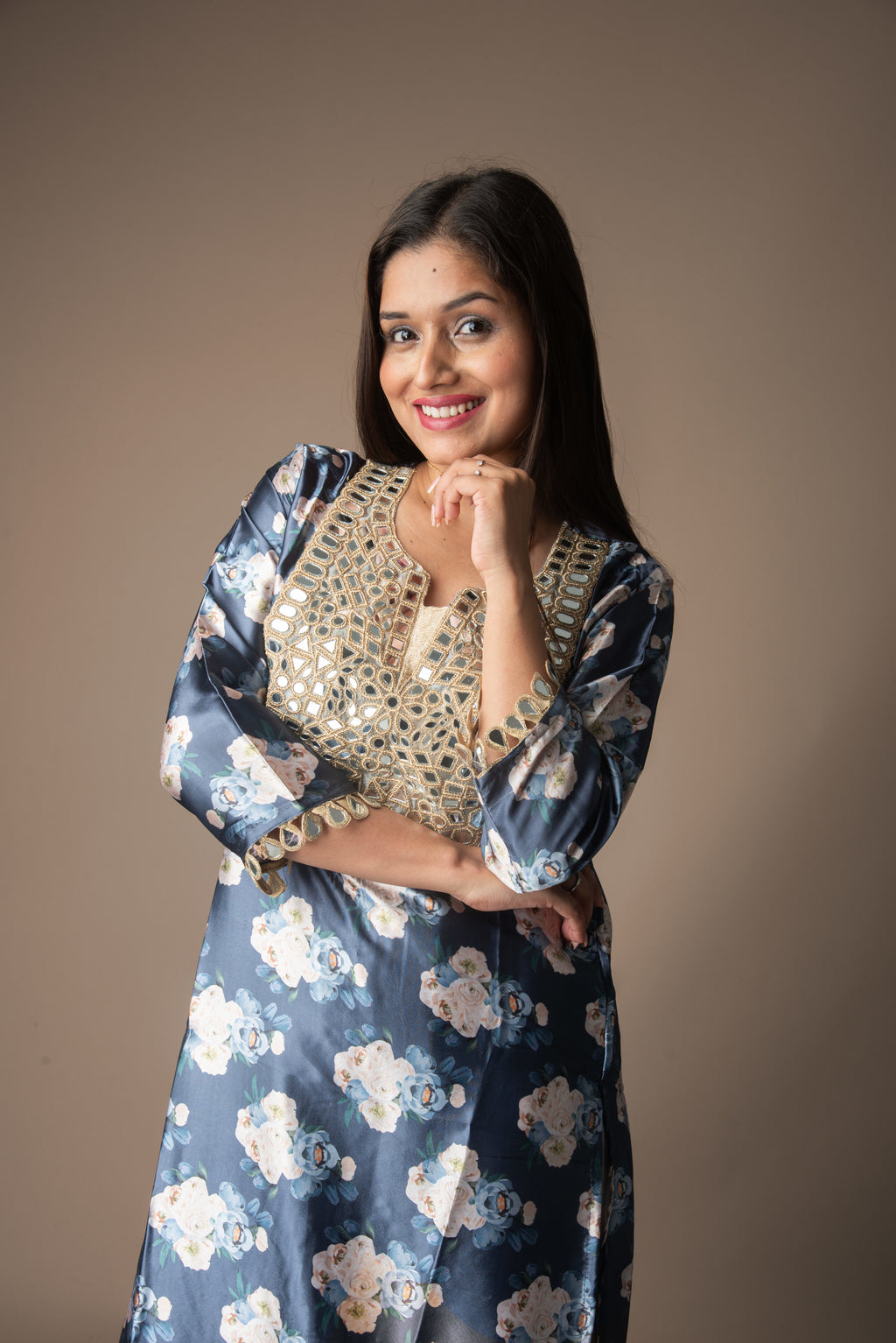 Woman wearing a blue floral dress with a beige top against a brown background