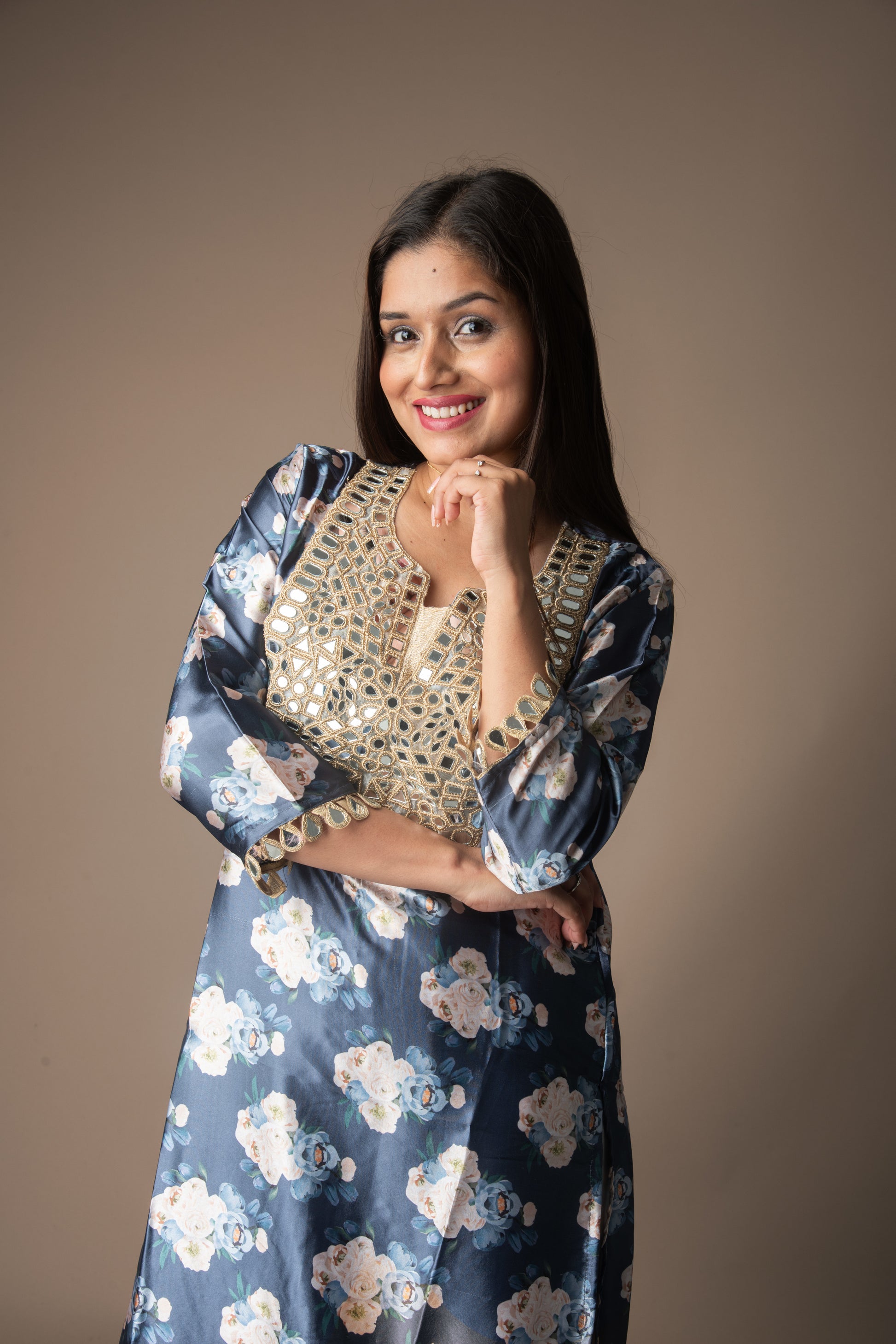 Woman wearing a blue floral dress with a beige top against a brown background