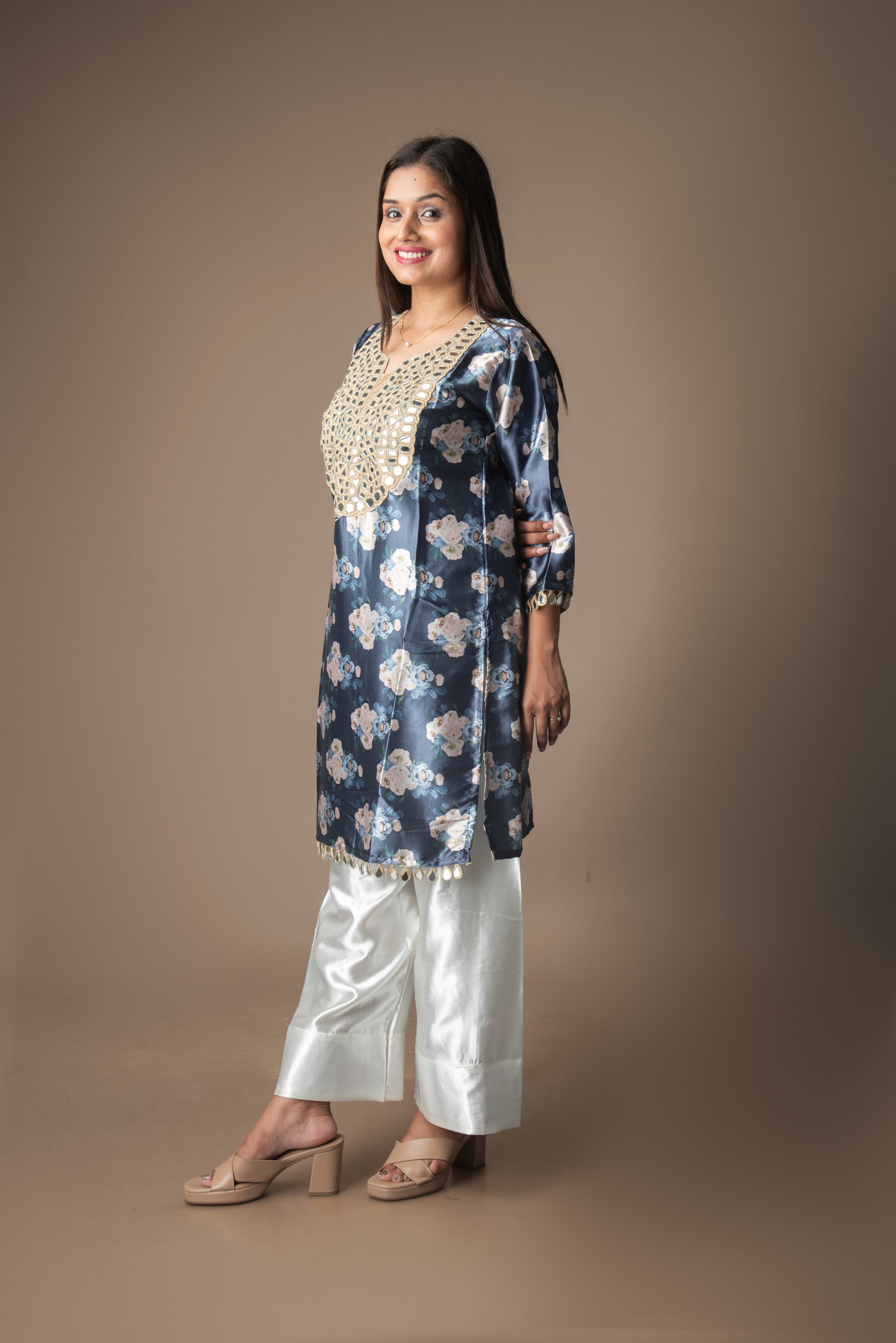 Woman wearing a floral kurta with white pants against a brown background