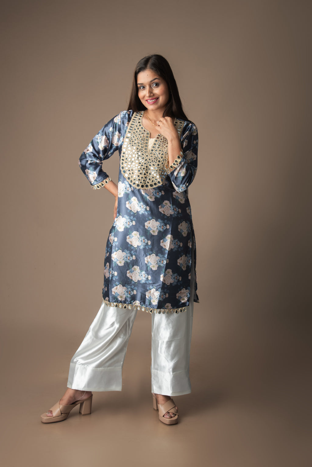 Woman wearing a blue floral kurta with white pants on a brown background