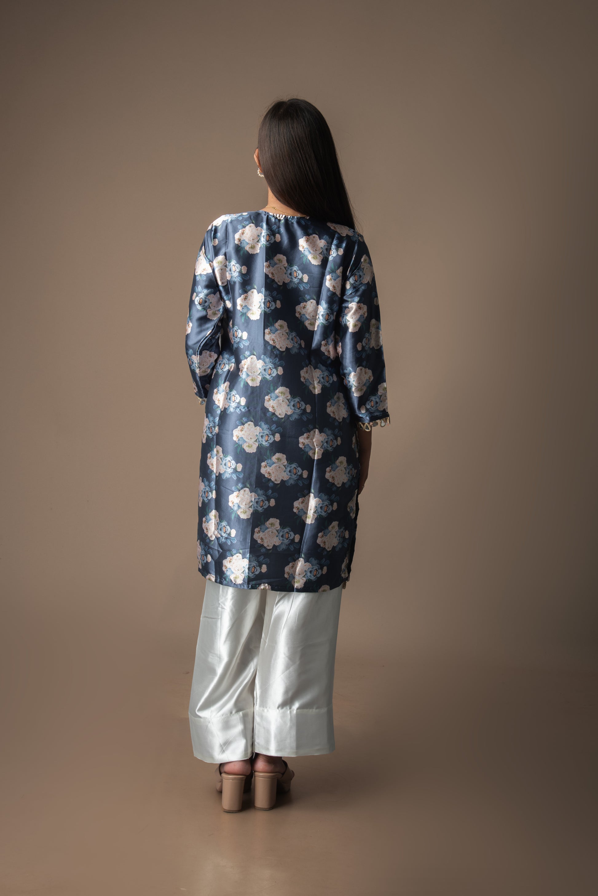 Person wearing a blue floral dress with white pants on a brown background