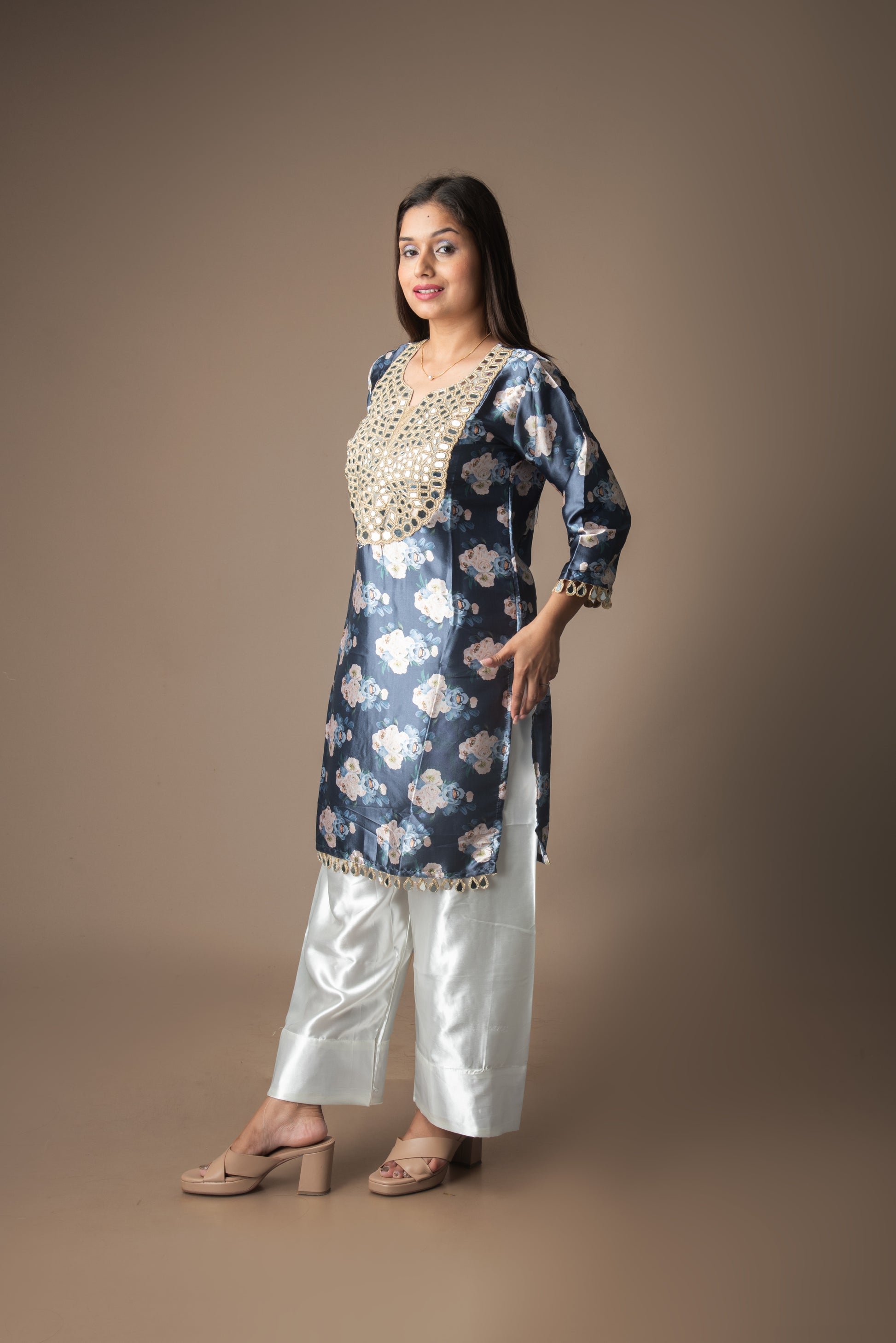 Woman wearing a blue floral kurta with white pants on a brown background