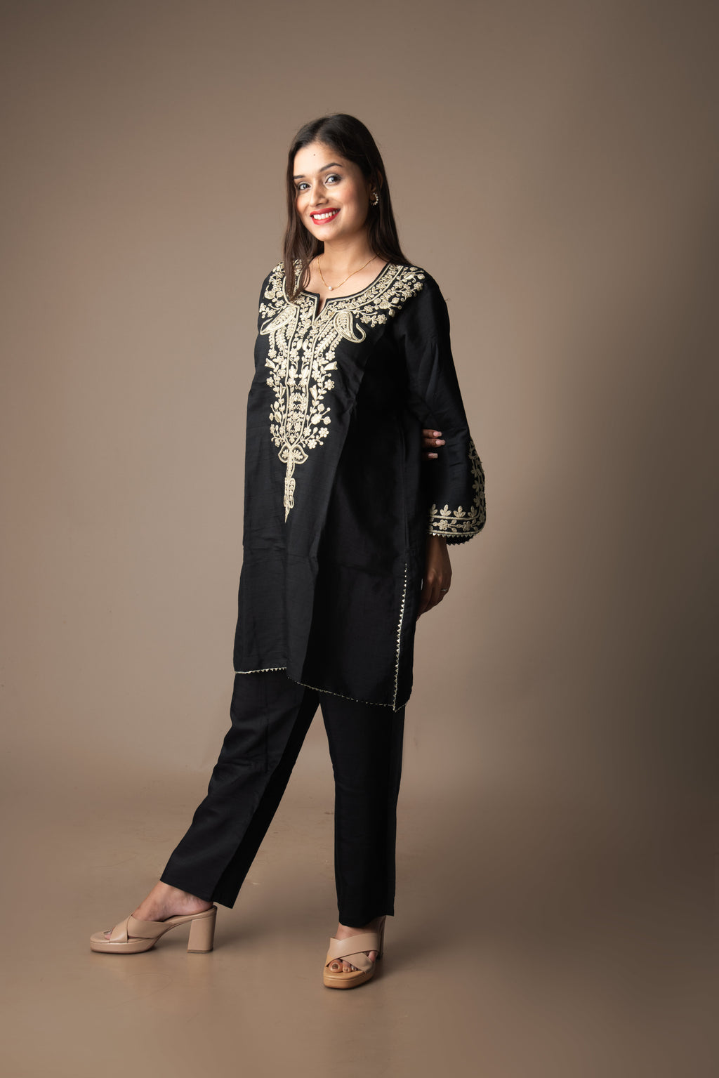 Woman wearing a black outfit with intricate white embroidery on a brown background