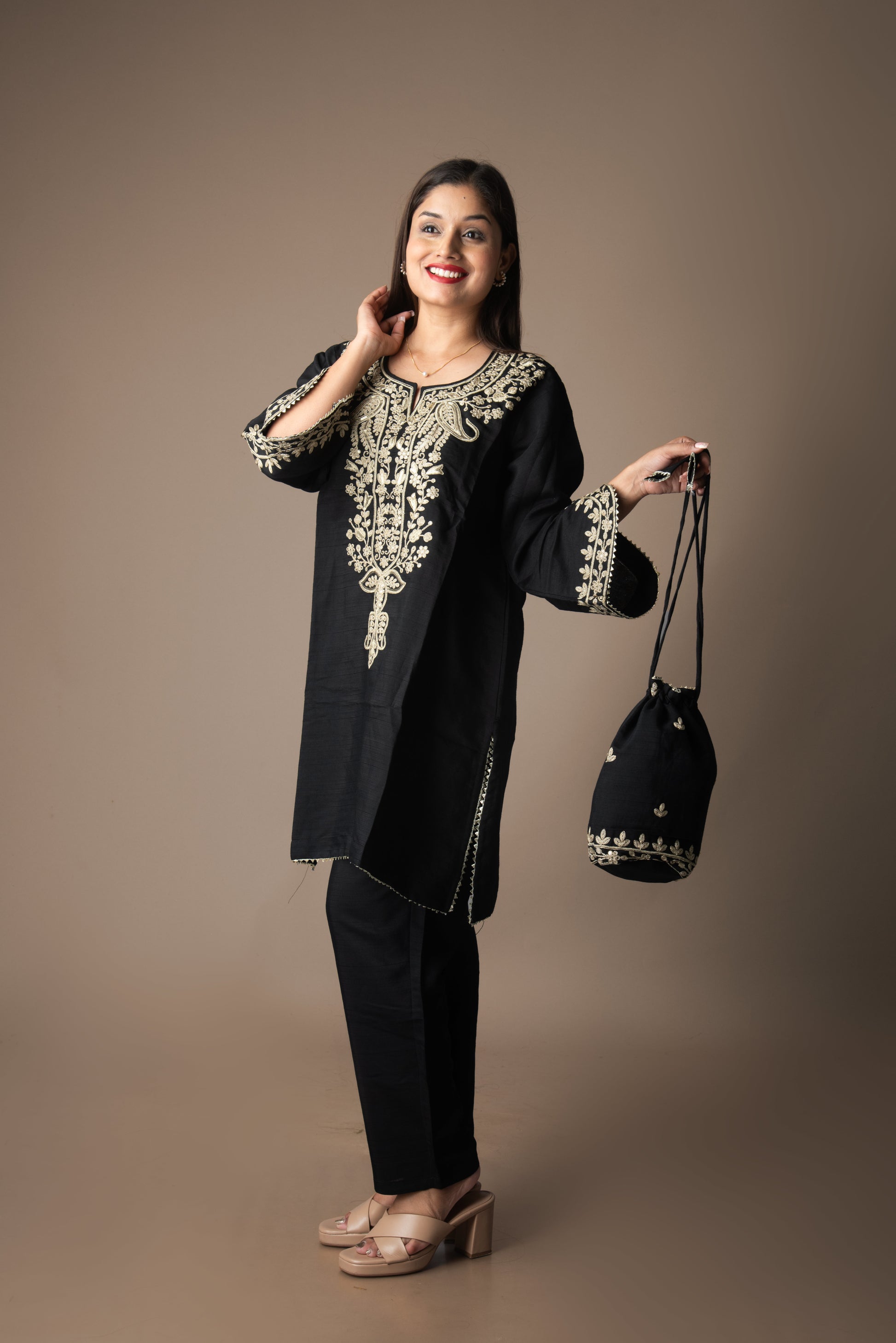 Woman wearing a black embroidered outfit holding a matching bag against a brown background