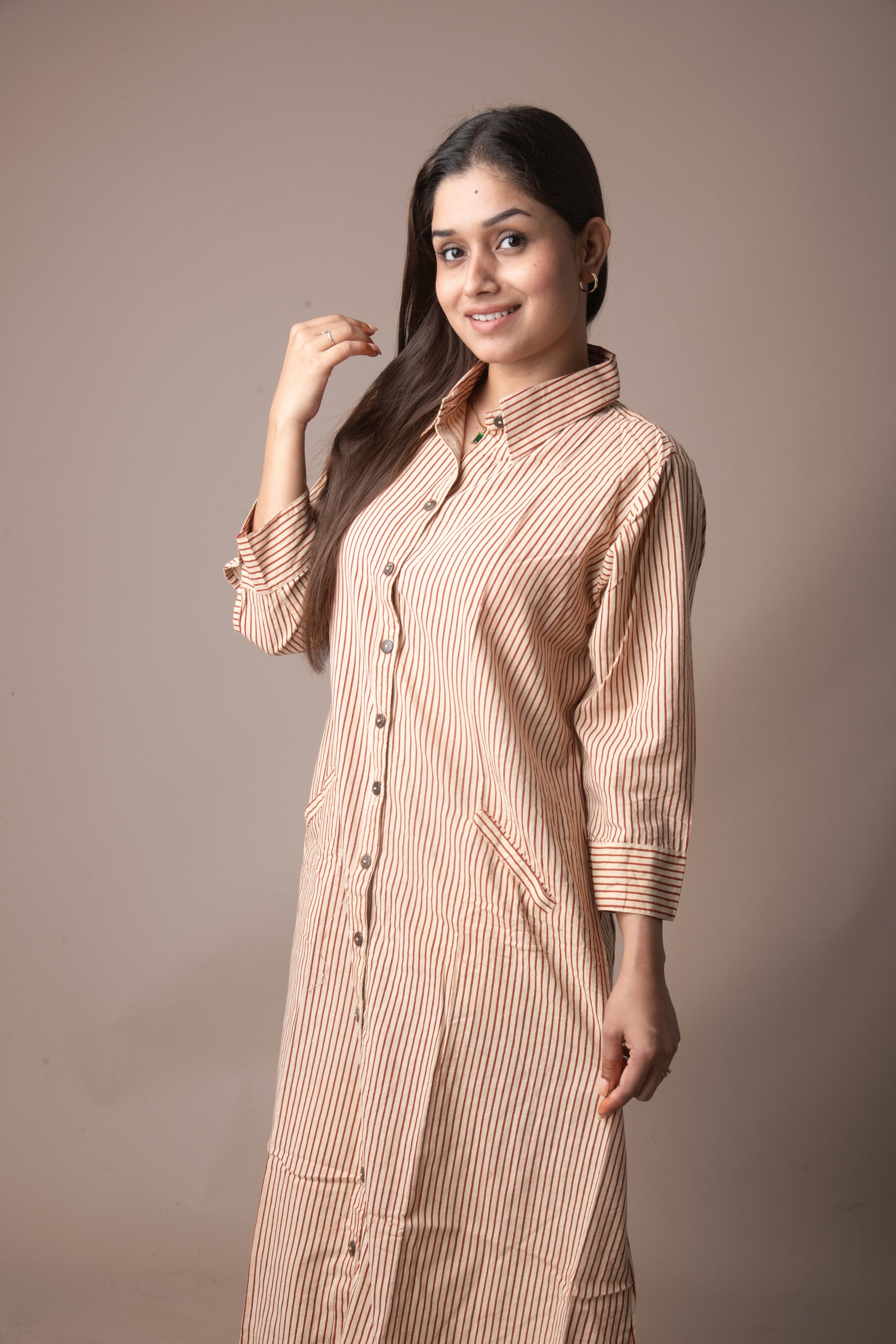 Woman wearing a long, light brown striped shirt against a plain background