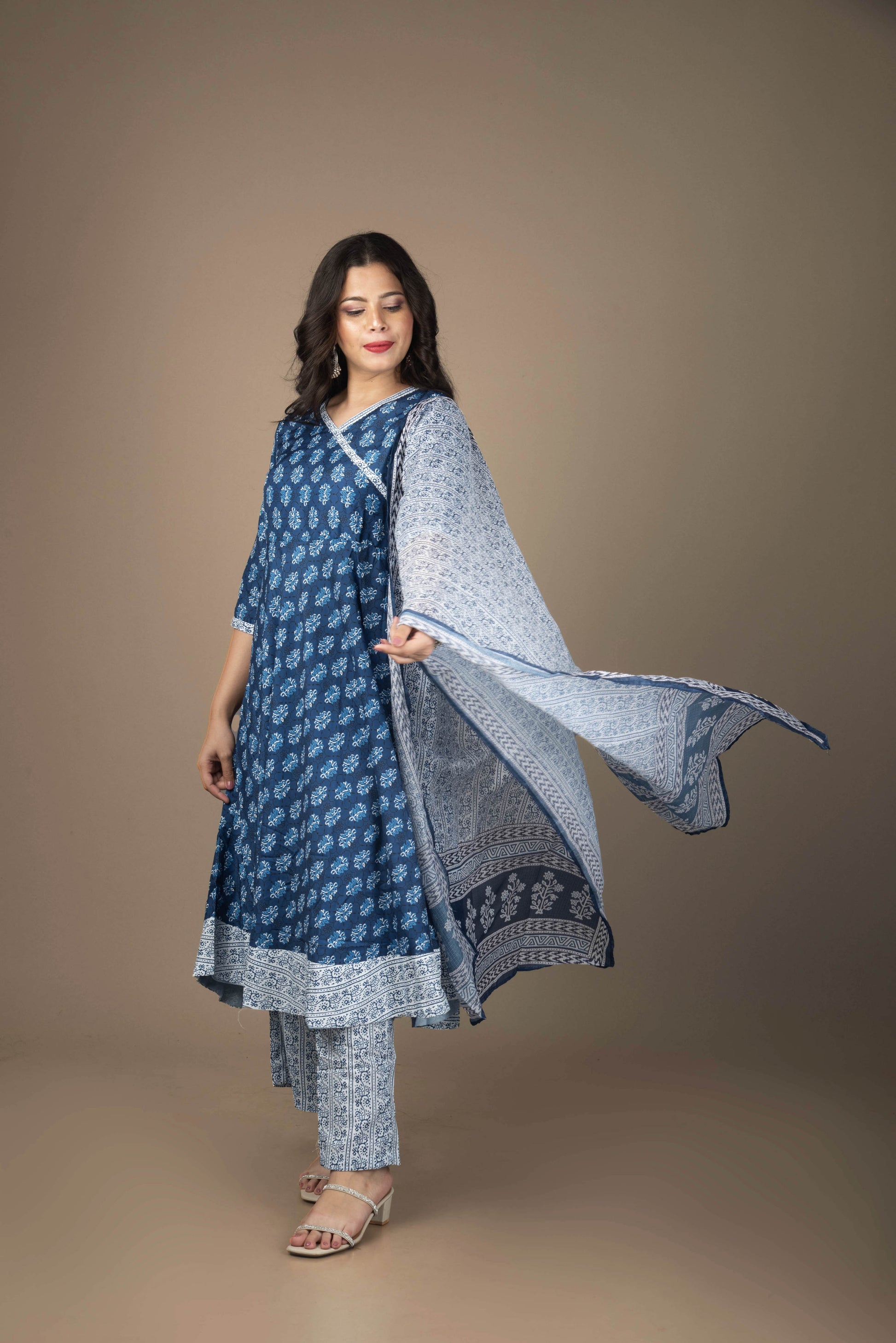 Woman wearing a blue and white traditional outfit with a shawl against a brown background