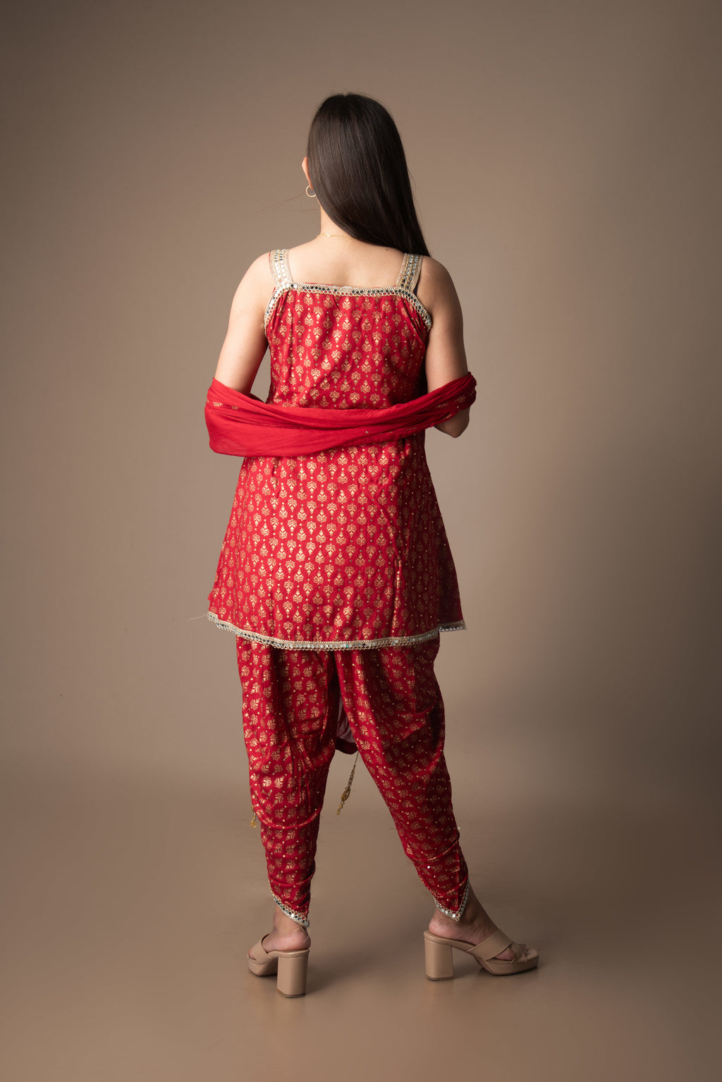 Woman wearing a red traditional outfit with a matching dupatta against a brown background