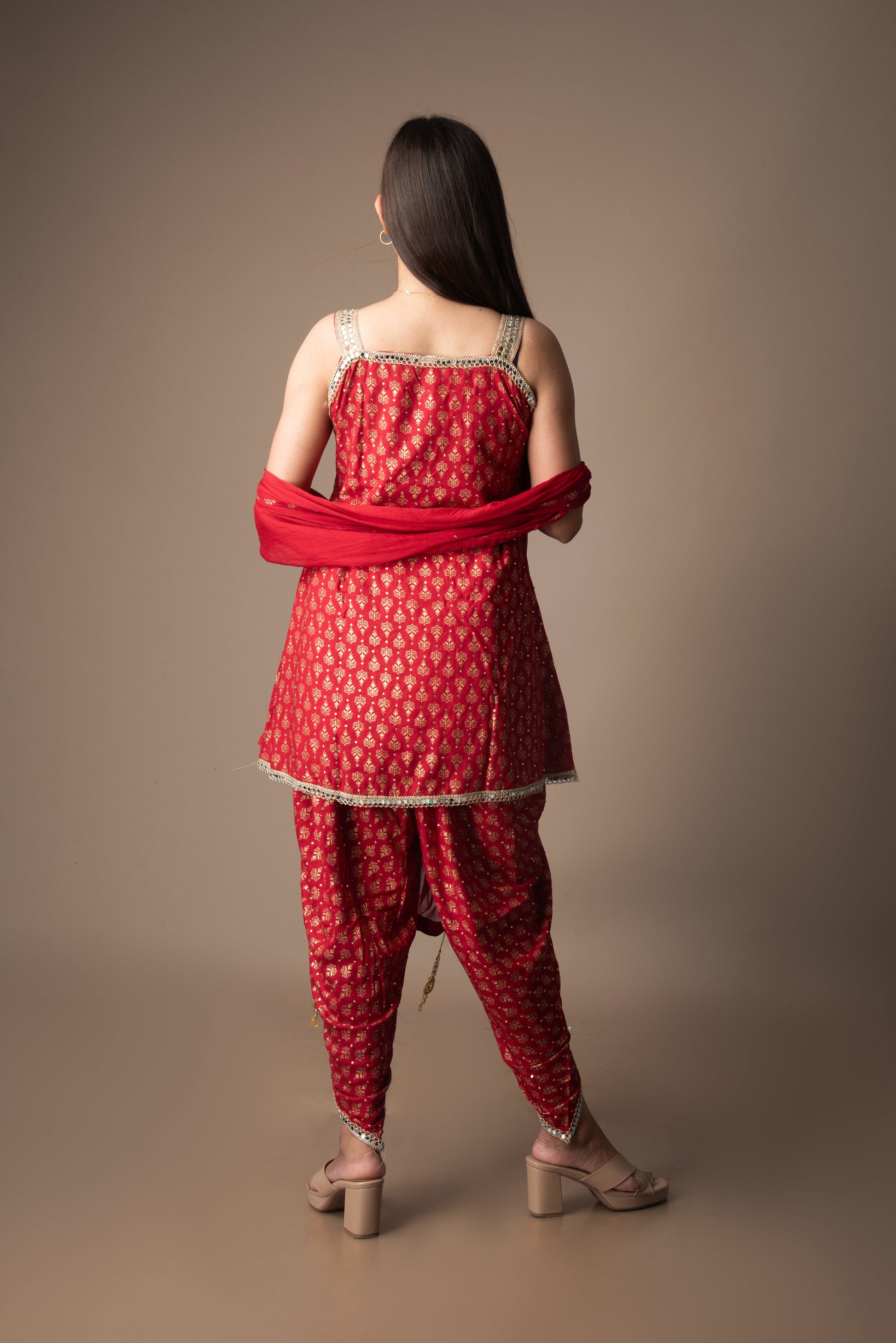Woman wearing a red traditional outfit with a matching dupatta against a brown background