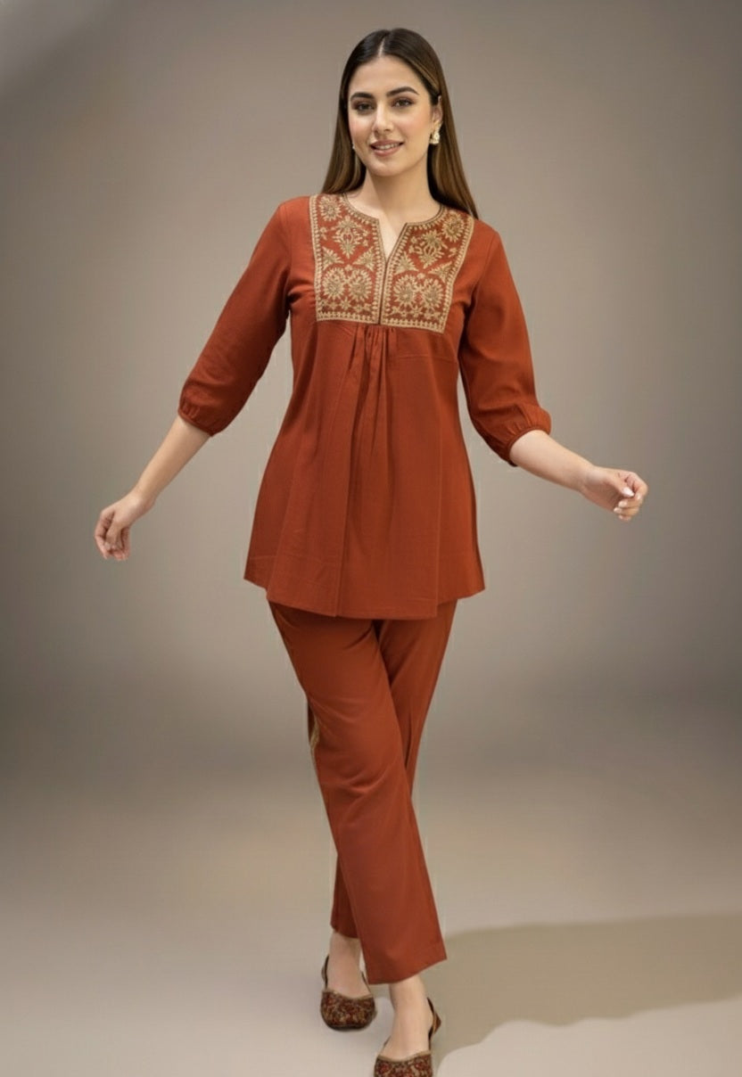 Woman wearing a rust-colored traditional outfit with intricate embroidery on a plain background