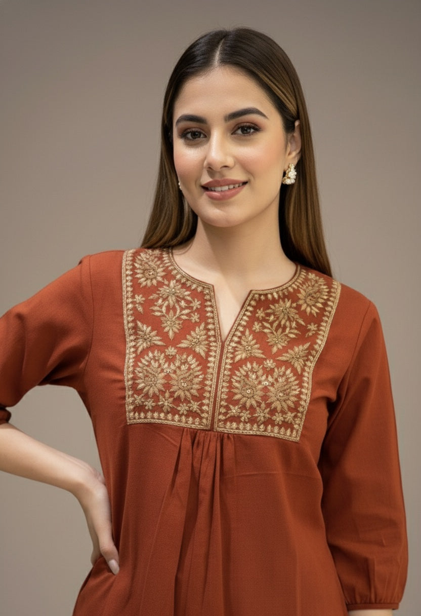 Woman wearing a rust-colored kurta with intricate embroidery on a plain background