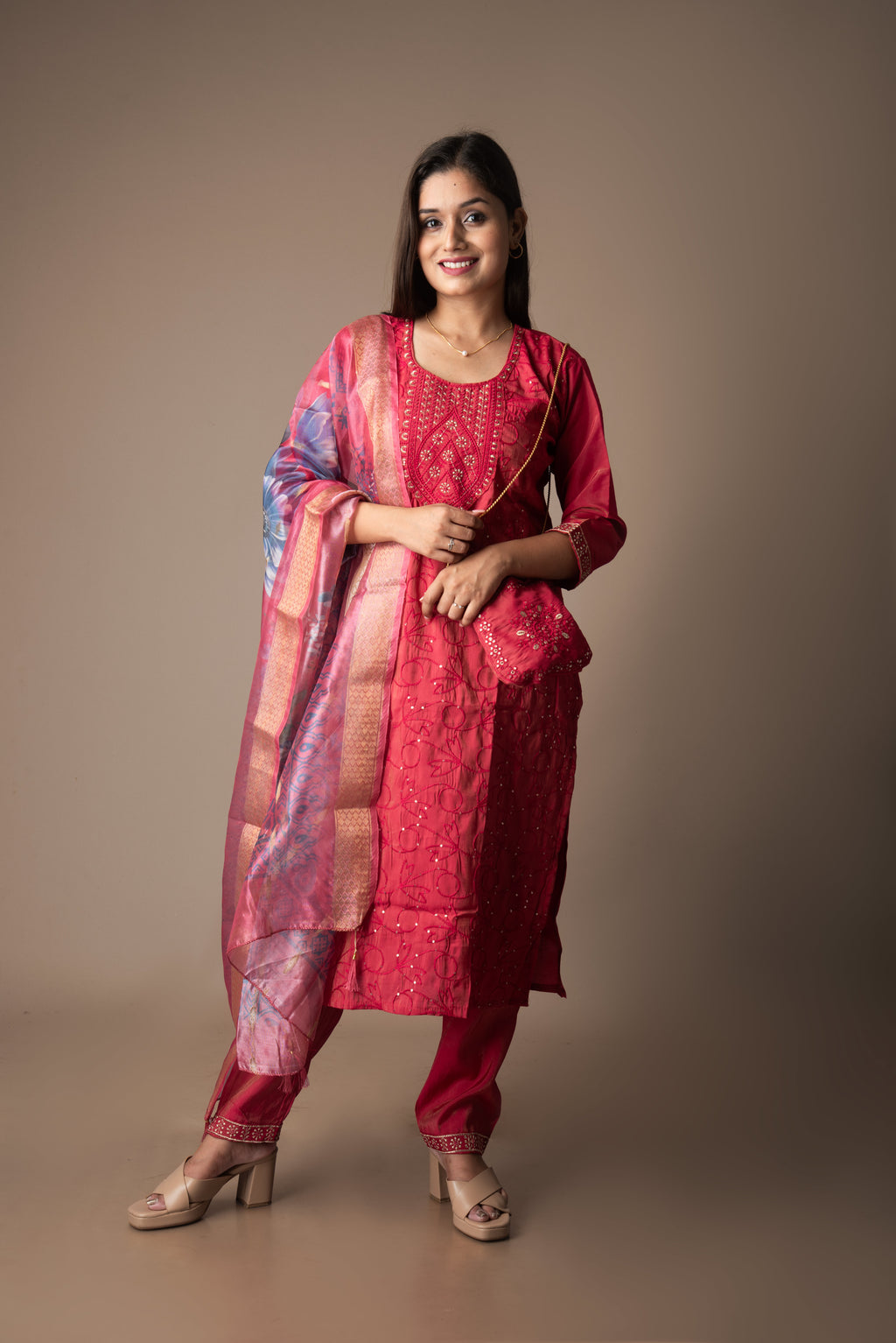 Woman wearing a red traditional outfit with a pink dupatta against a brown background