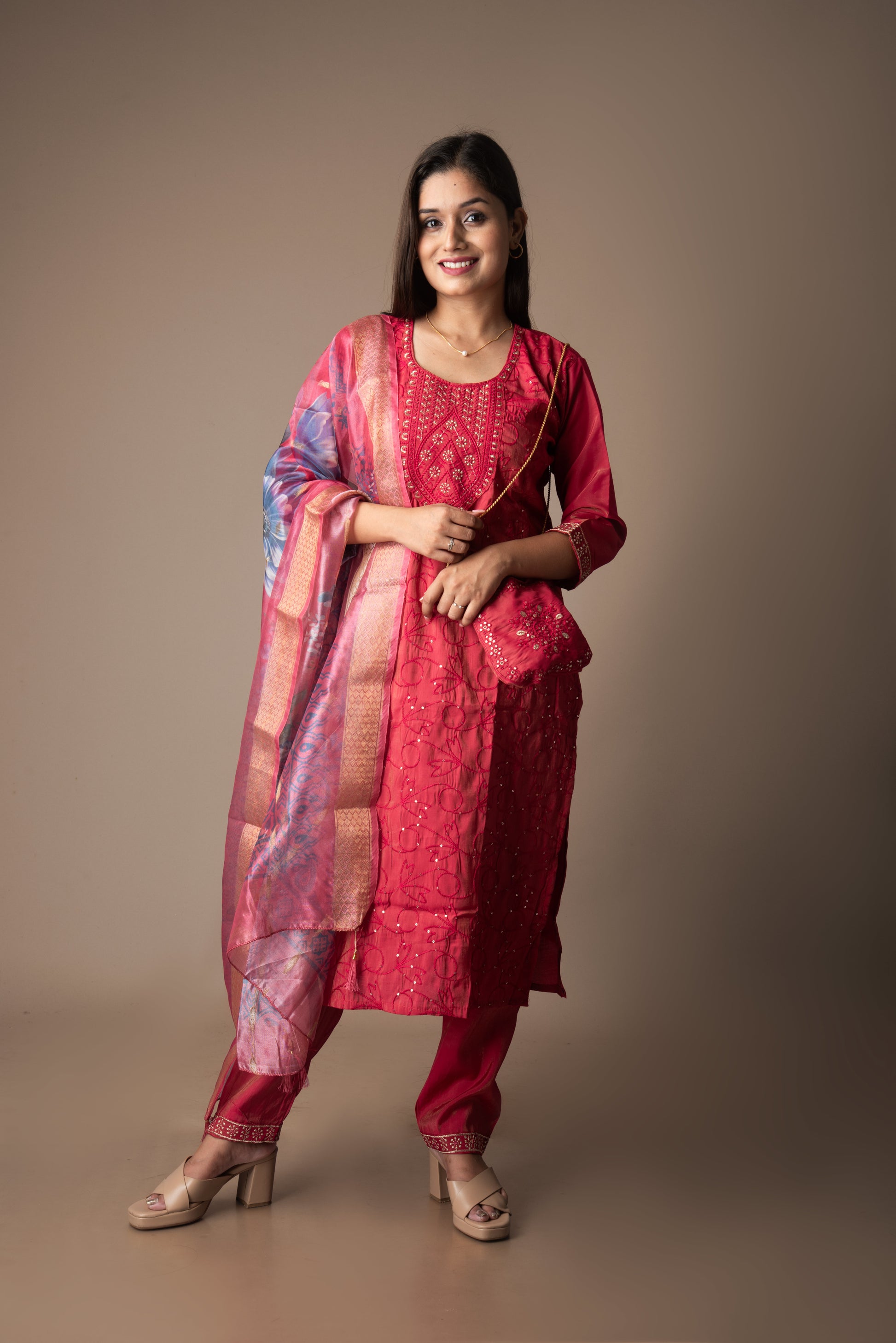 Woman wearing a red traditional outfit with a pink dupatta against a brown background