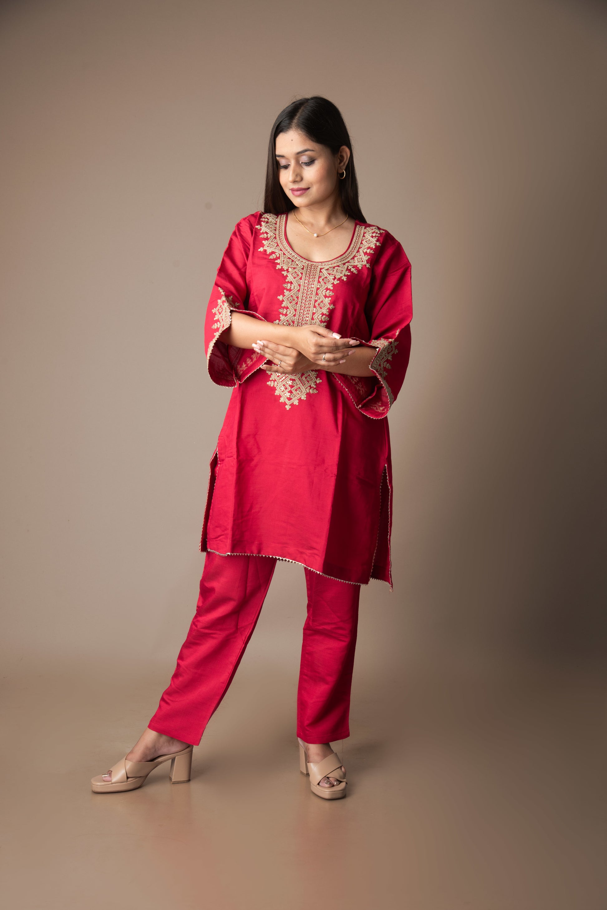 Woman wearing a red traditional outfit with intricate embroidery on a brown background