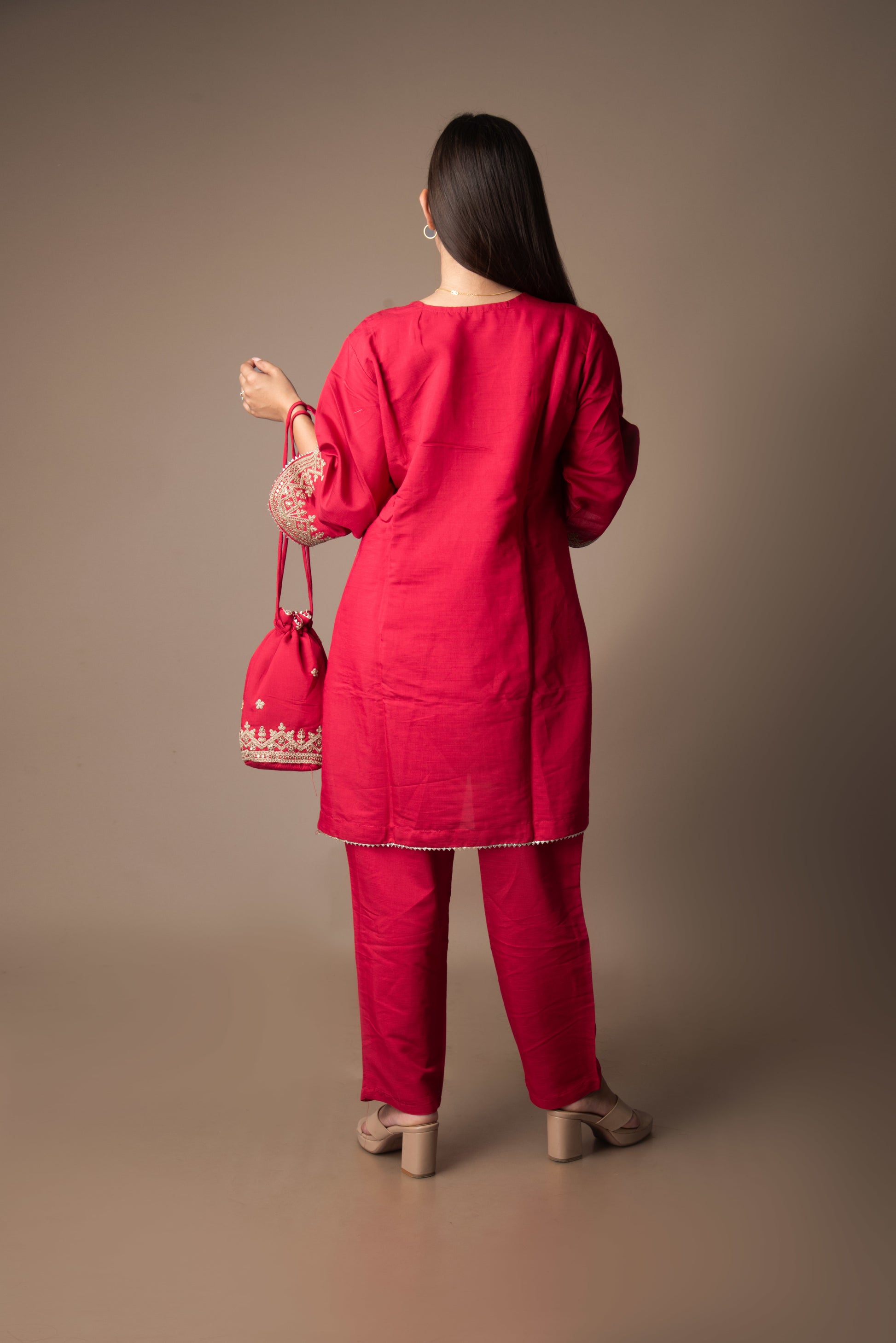 Woman in a red traditional outfit holding a pink bag against a brown background