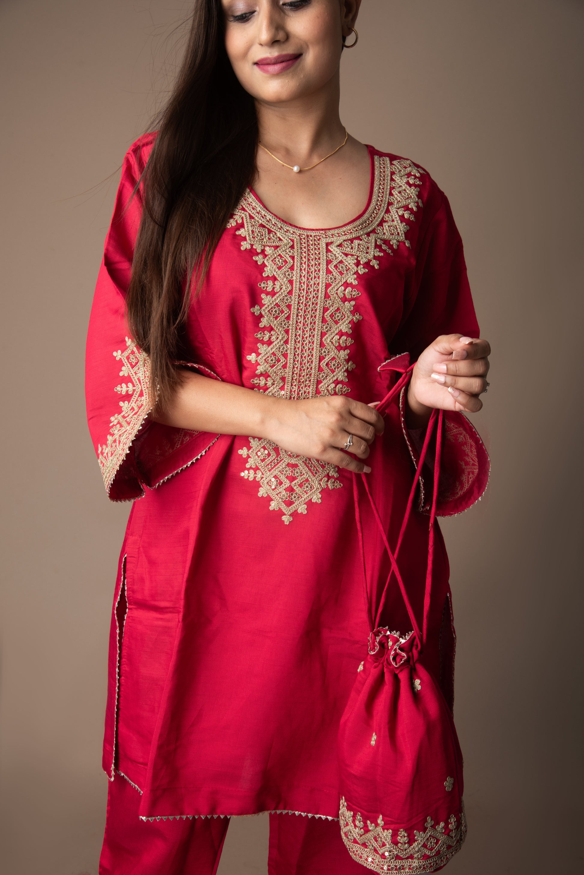 Woman wearing a red embroidered outfit holding a matching bag against a brown background