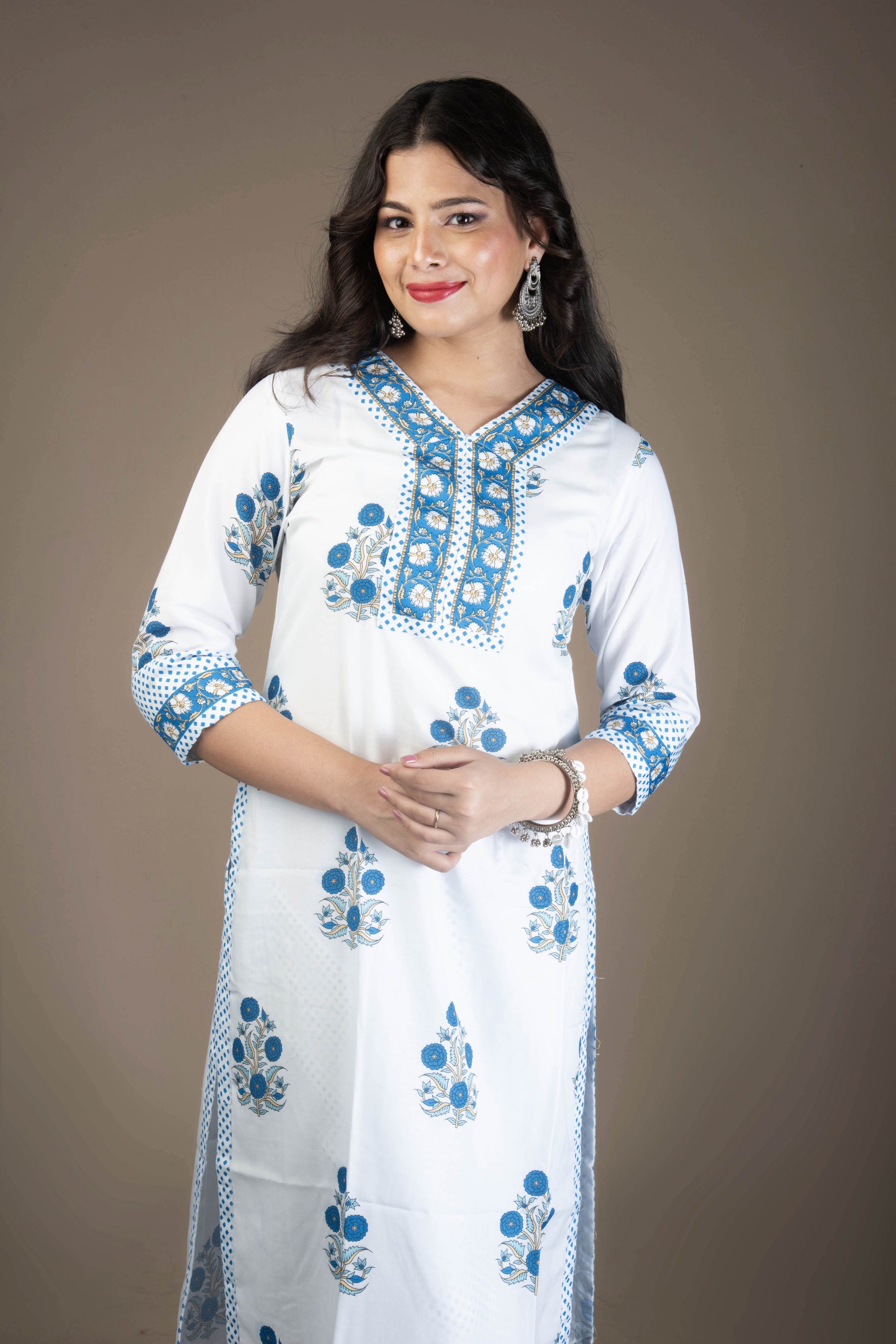 Woman wearing a white kurta with blue embroidery on a brown background