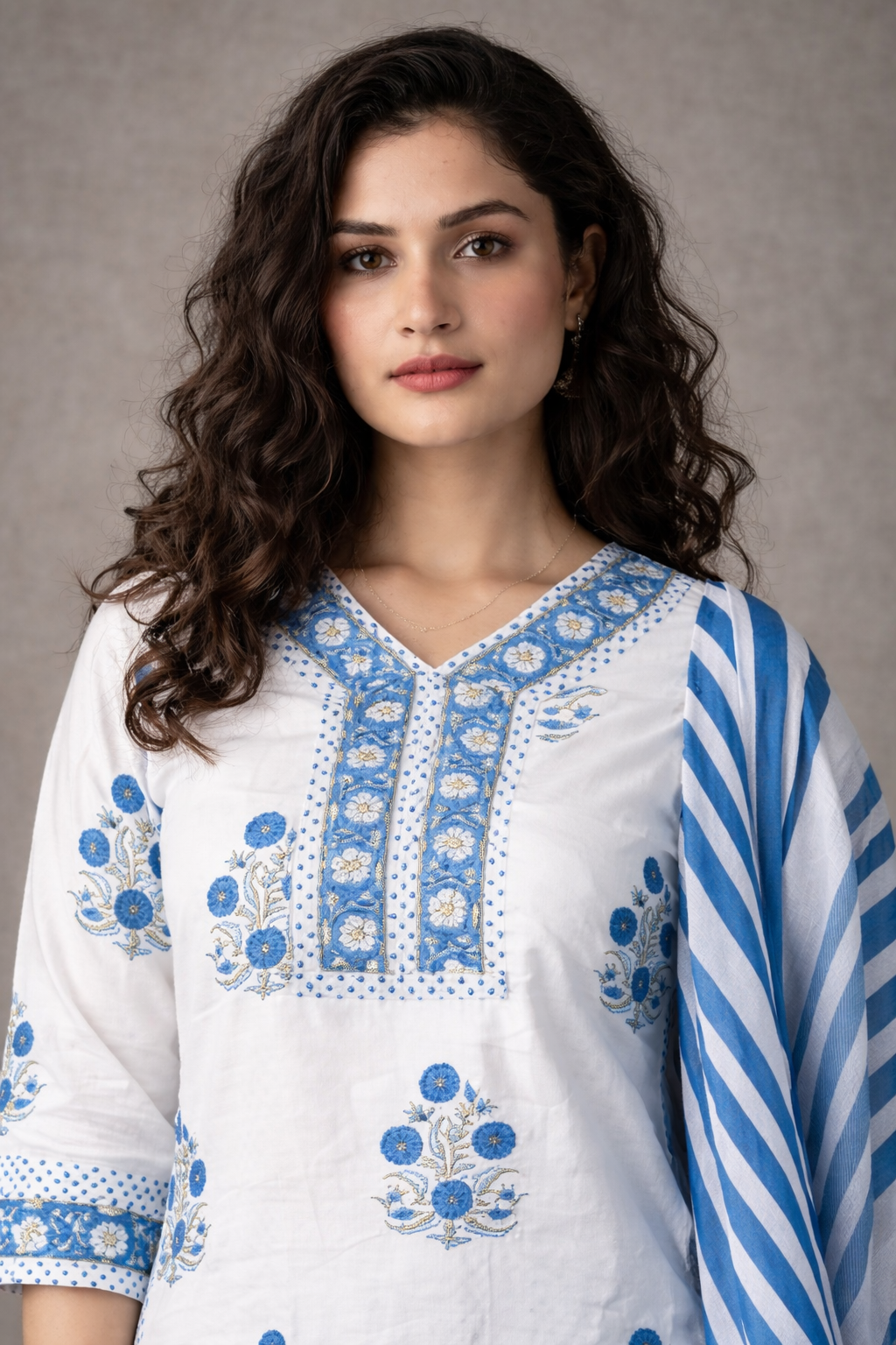 Woman wearing a white embroidered top with blue patterns and a matching scarf against a gray background