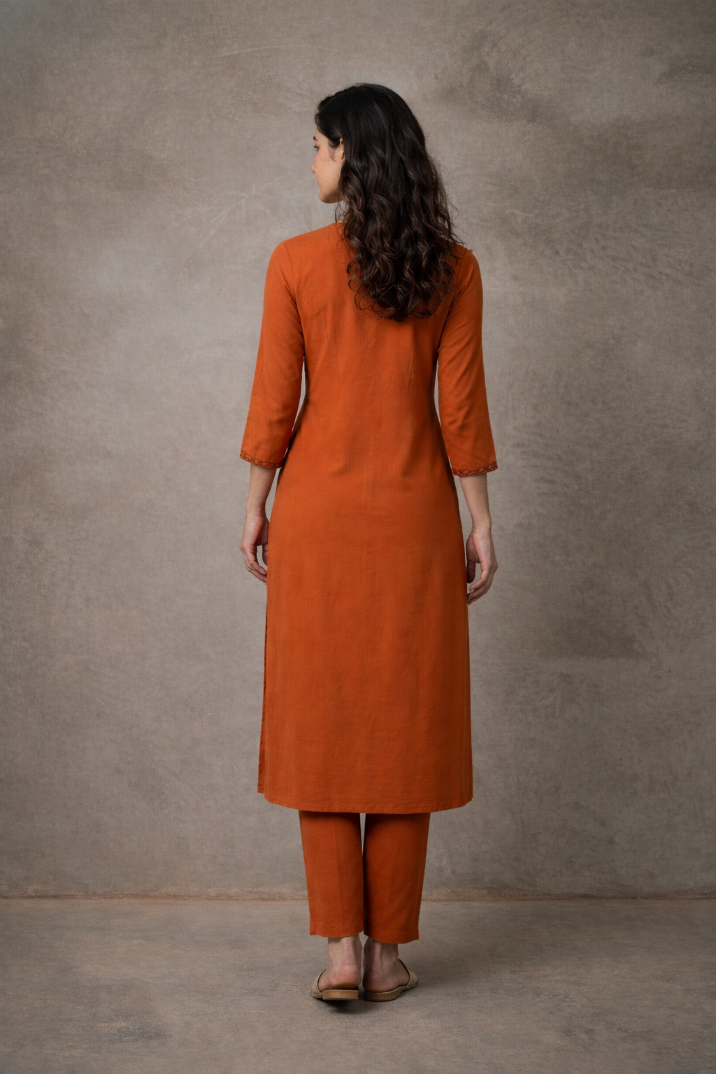Woman wearing an orange kurta with pants against a gray background