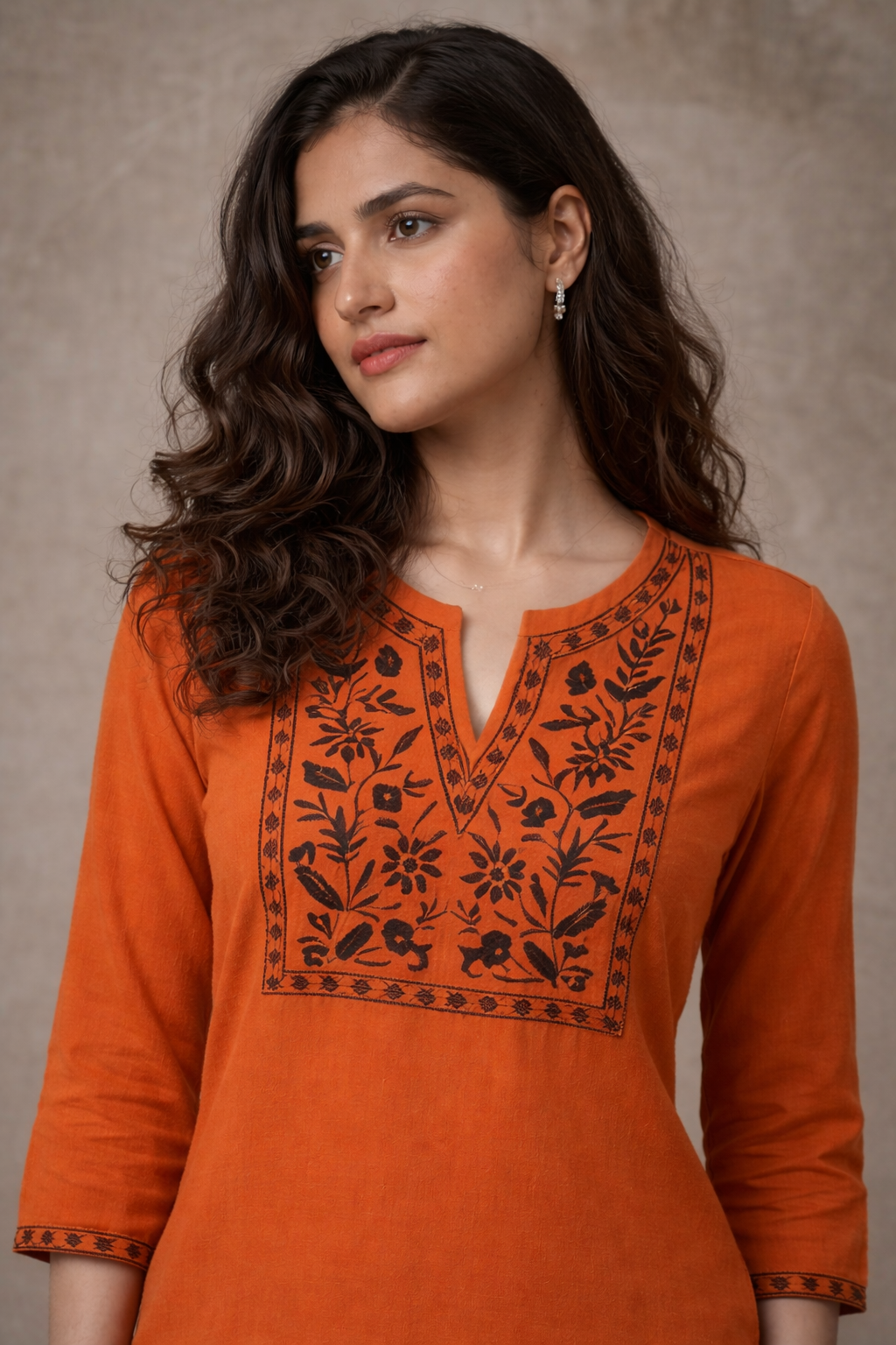 Woman wearing an orange kurta with black embroidery against a neutral background