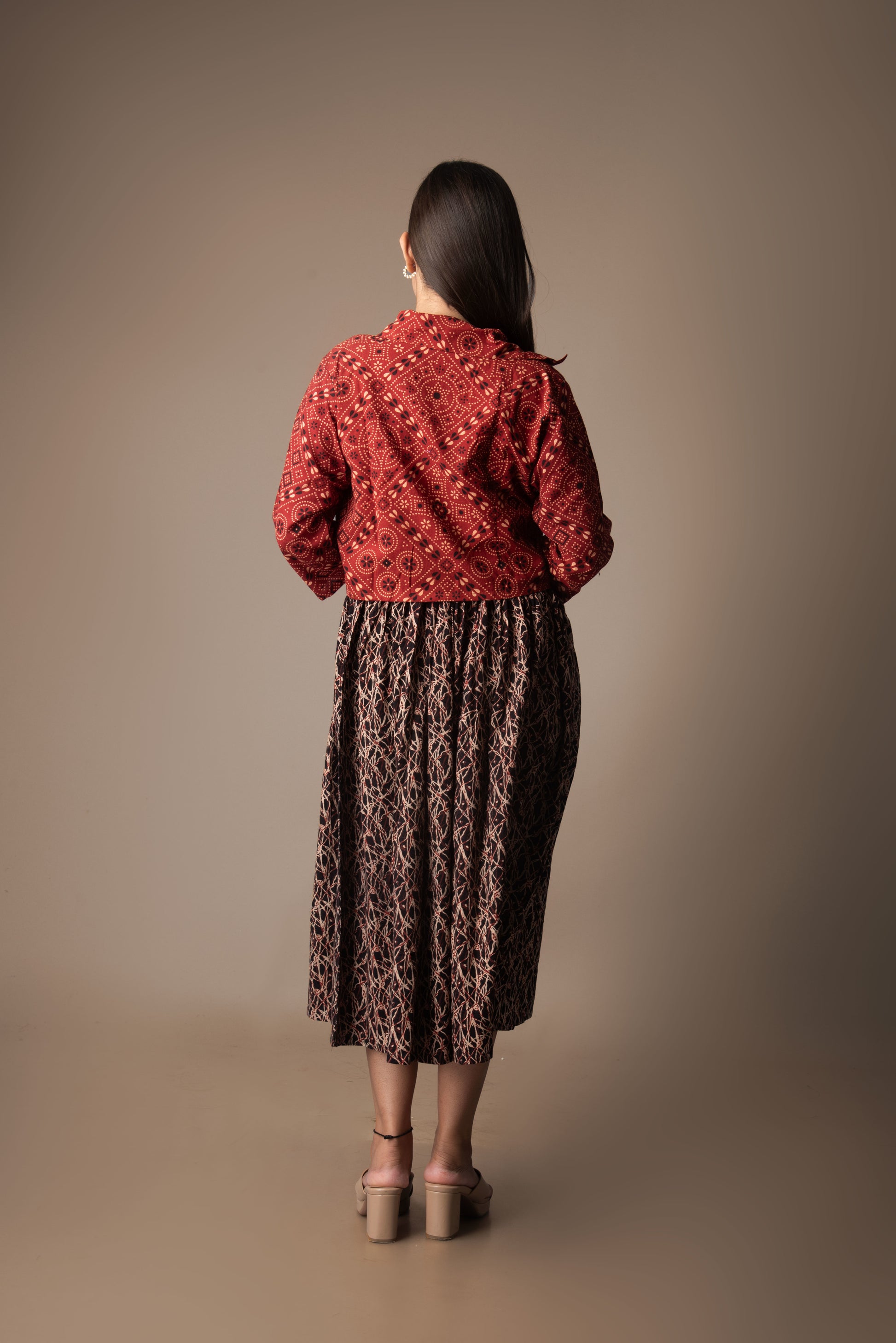 Woman wearing a red patterned blouse and brown skirt against a beige background