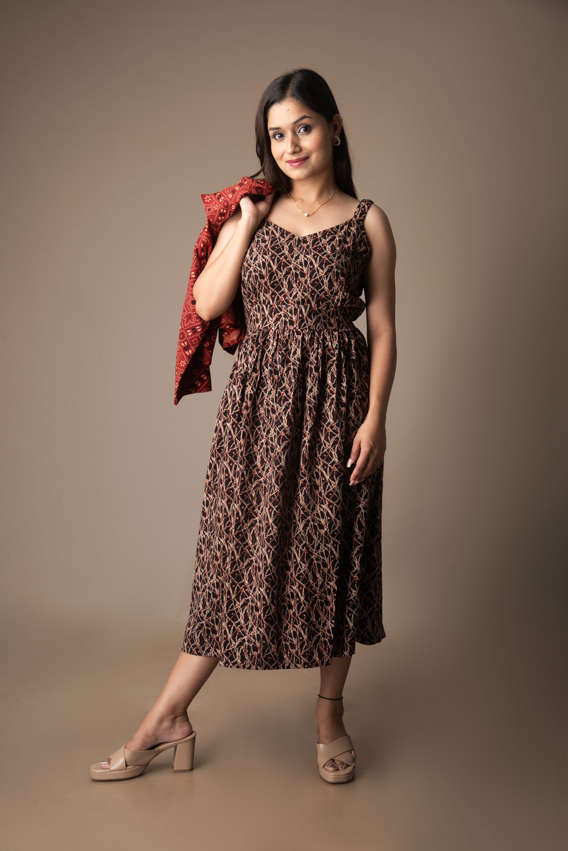 Woman wearing a leopard print dress holding a red jacket against a brown background