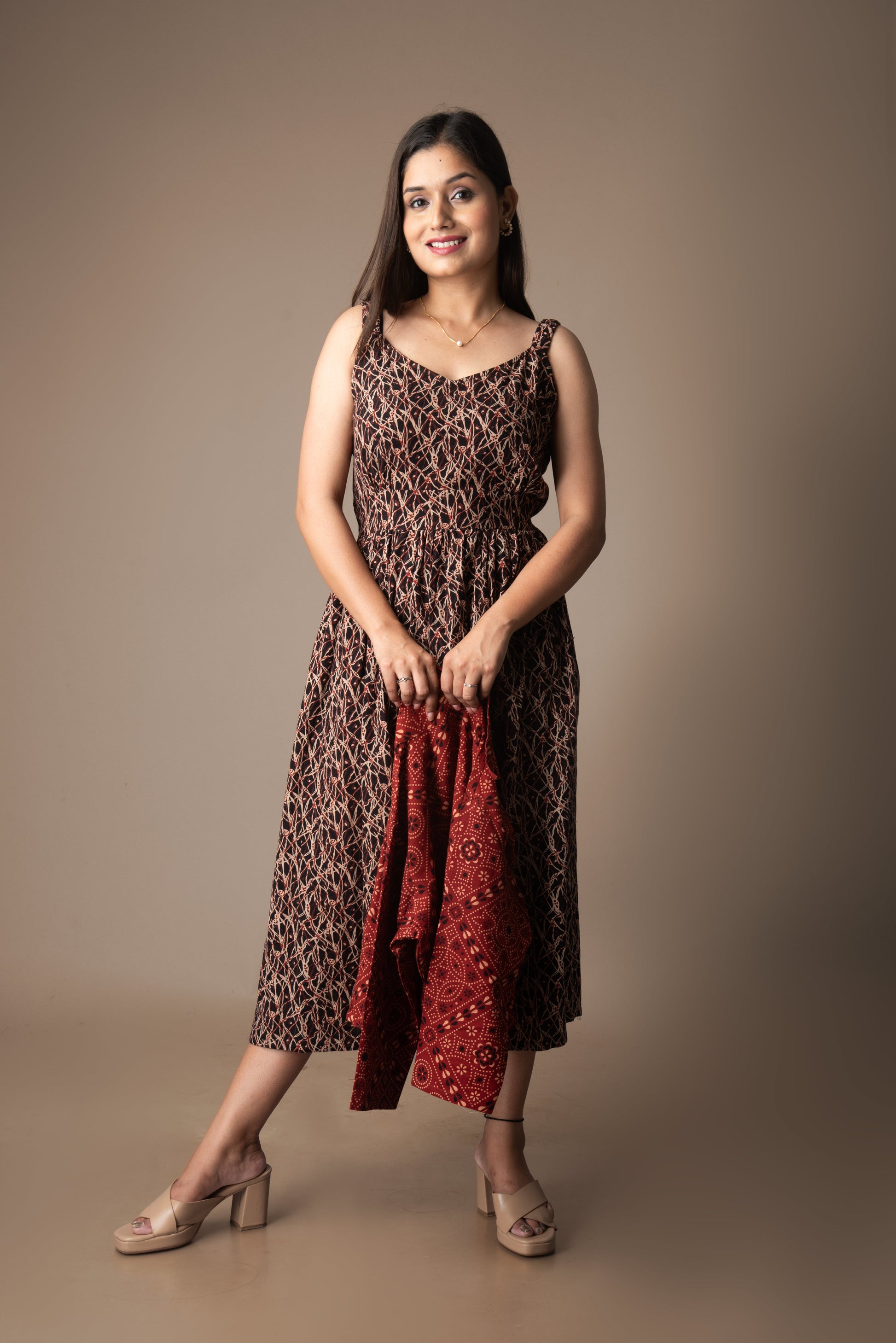 Woman wearing a patterned dress holding a red scarf against a brown background