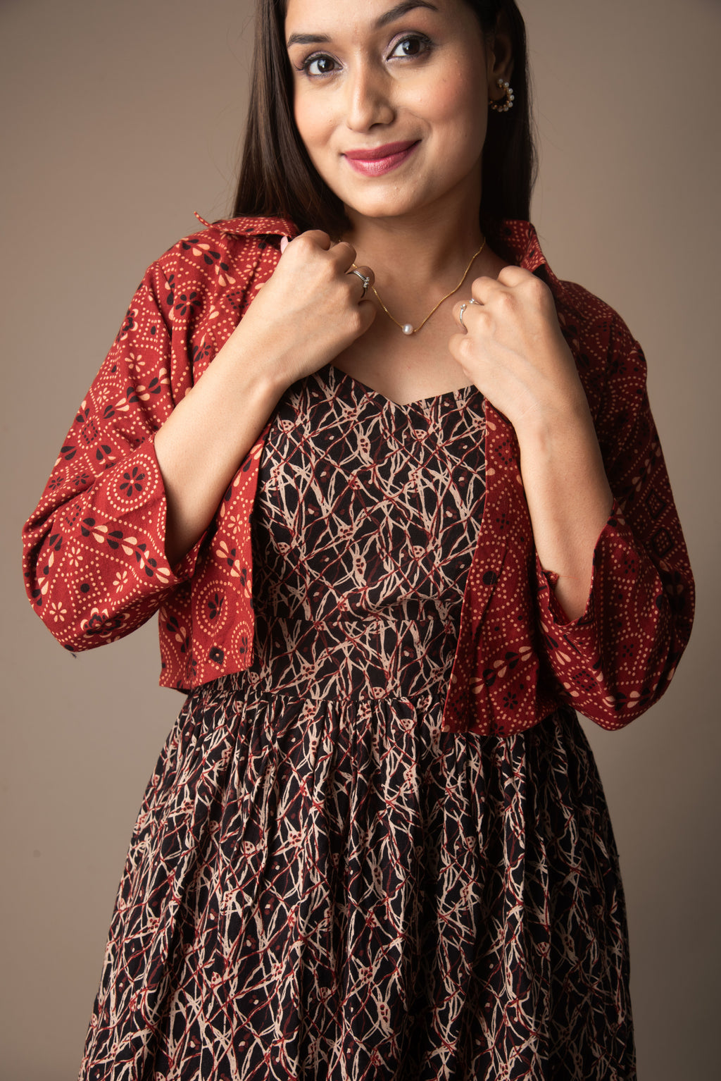 Woman wearing a red patterned top over a brown dress against a plain background