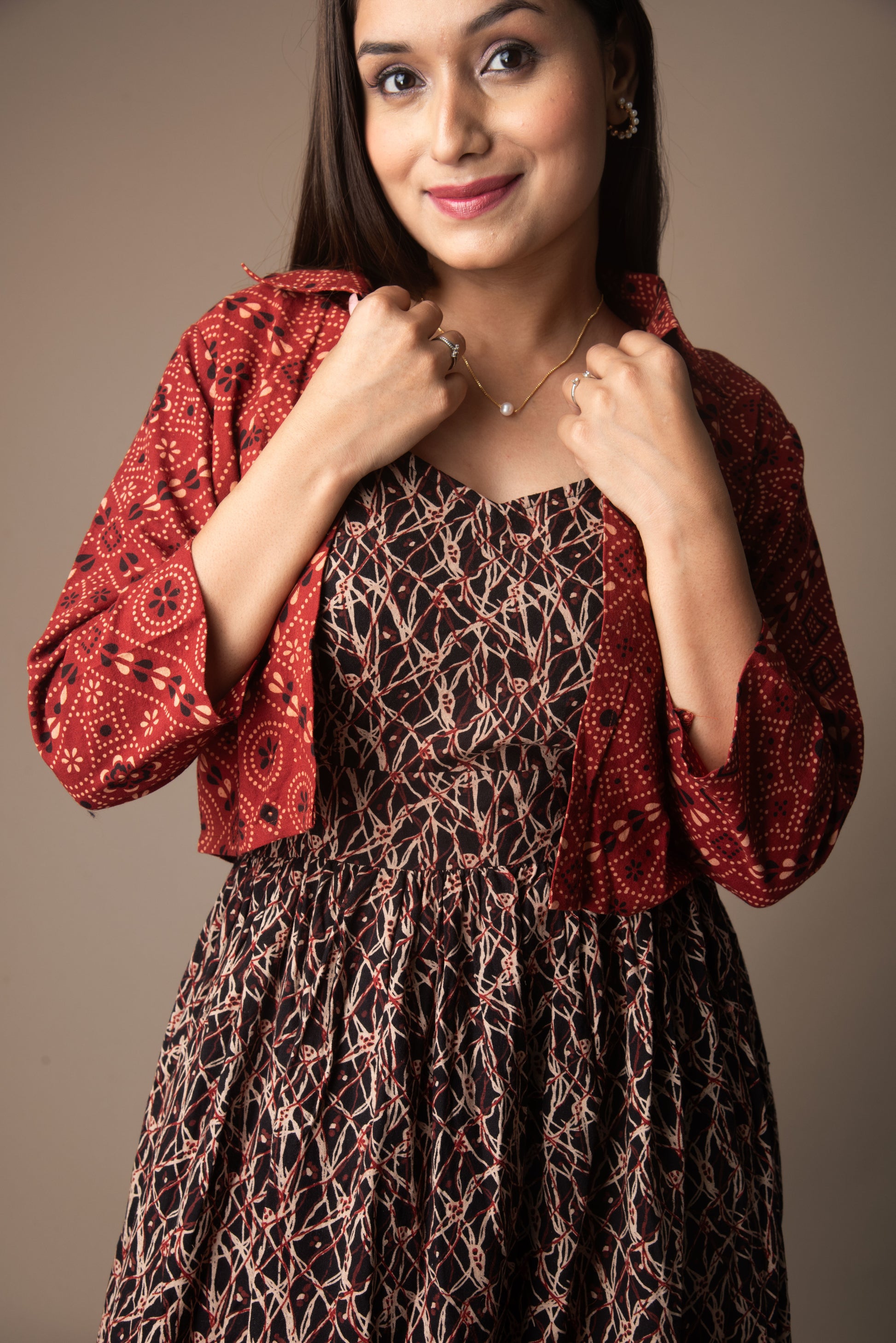 Woman wearing a red patterned top over a brown dress against a plain background
