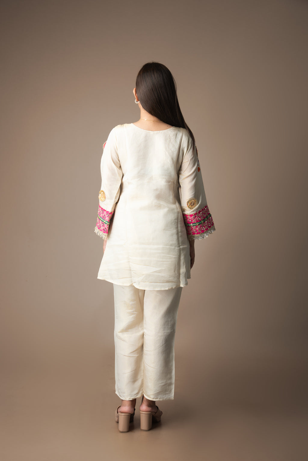 Woman wearing a cream kurta with pink and gold embroidery on a brown background