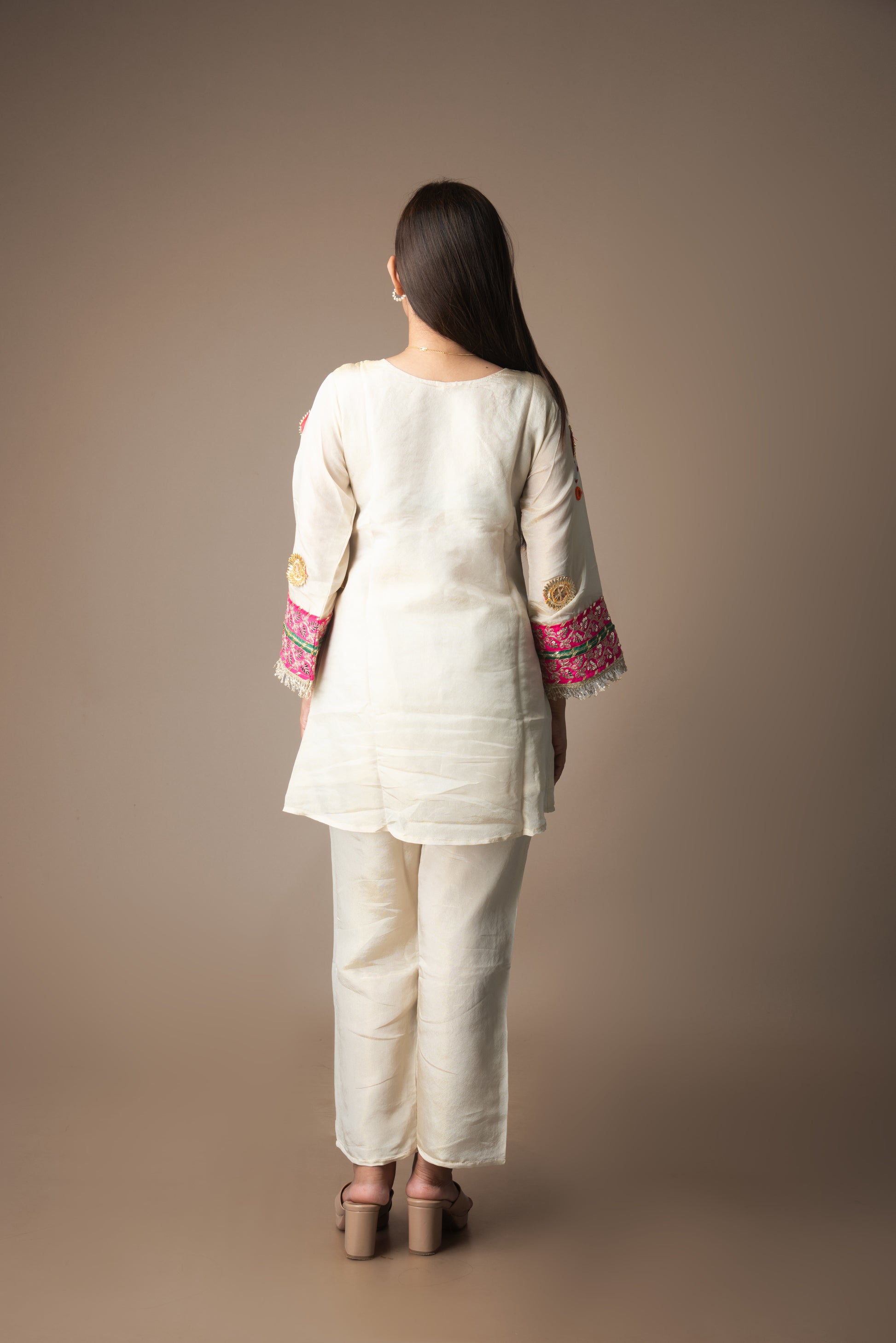 Woman wearing a cream kurta with pink and gold embroidery on a brown background