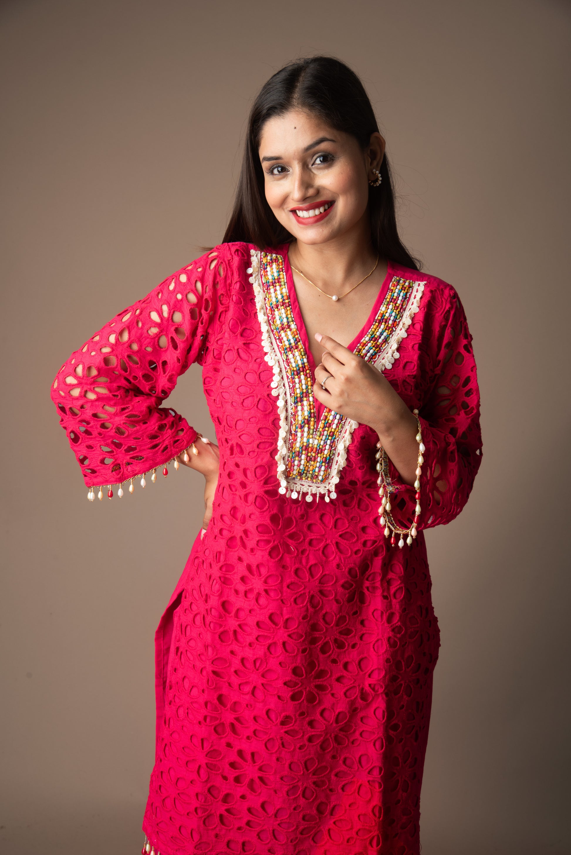 Woman wearing a bright pink traditional outfit with decorative elements on a brown background