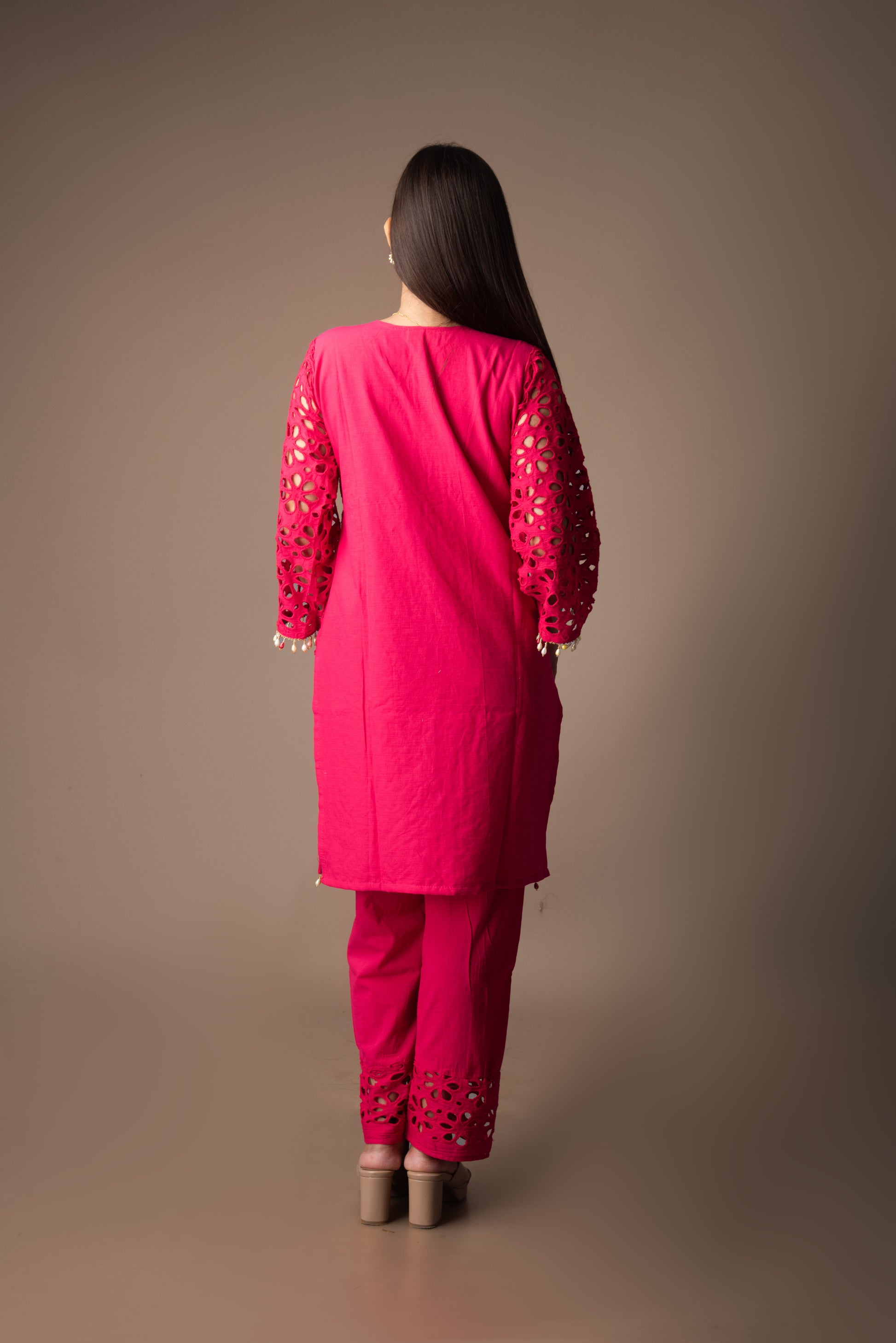 Woman wearing a bright pink traditional outfit with intricate designs on a brown background