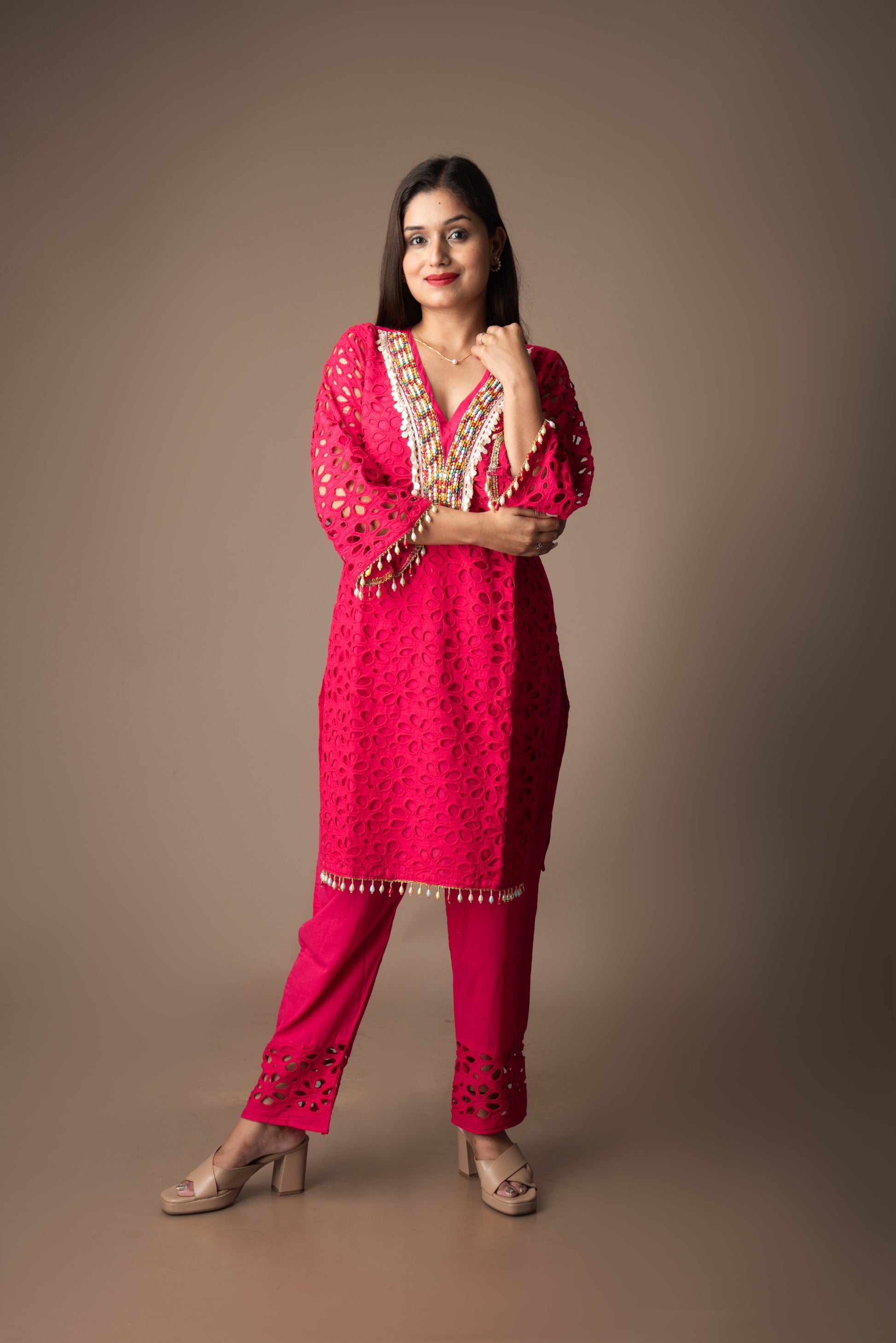 Woman wearing a pink traditional outfit with gold embroidery on a brown background