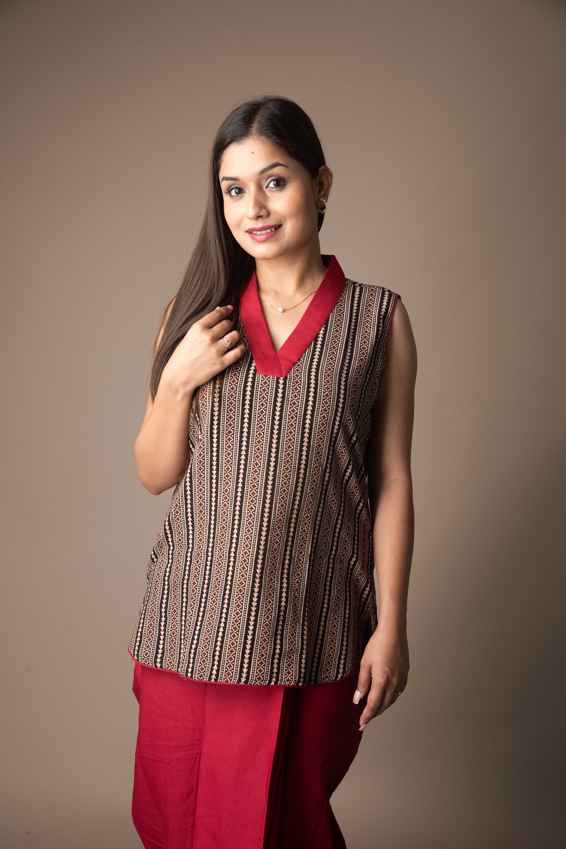 Woman wearing a sleeveless patterned top with a red collar and red pants on a brown background