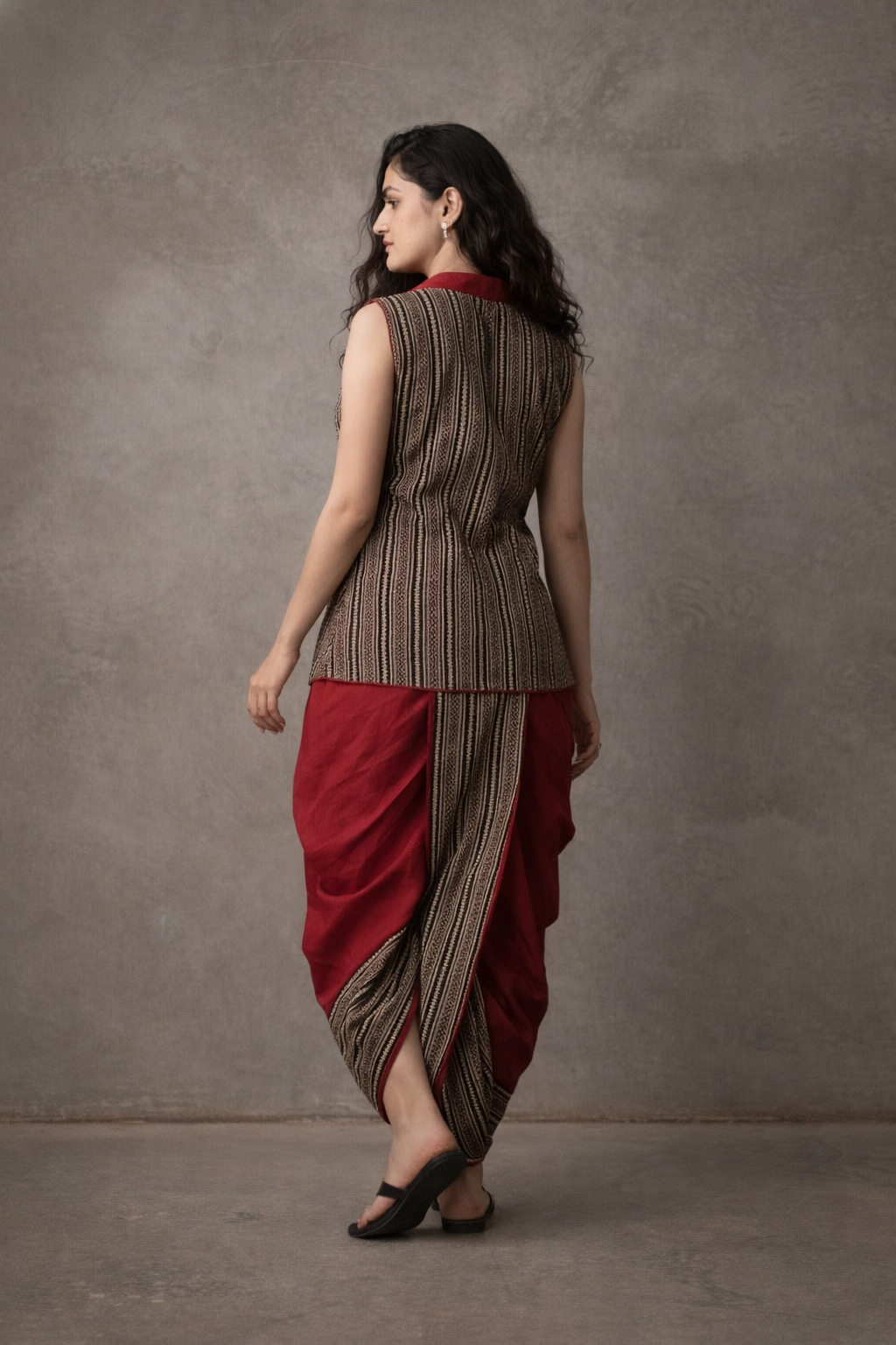 Woman wearing a sleeveless top and red and brown dhoti-style skirt against a gray background